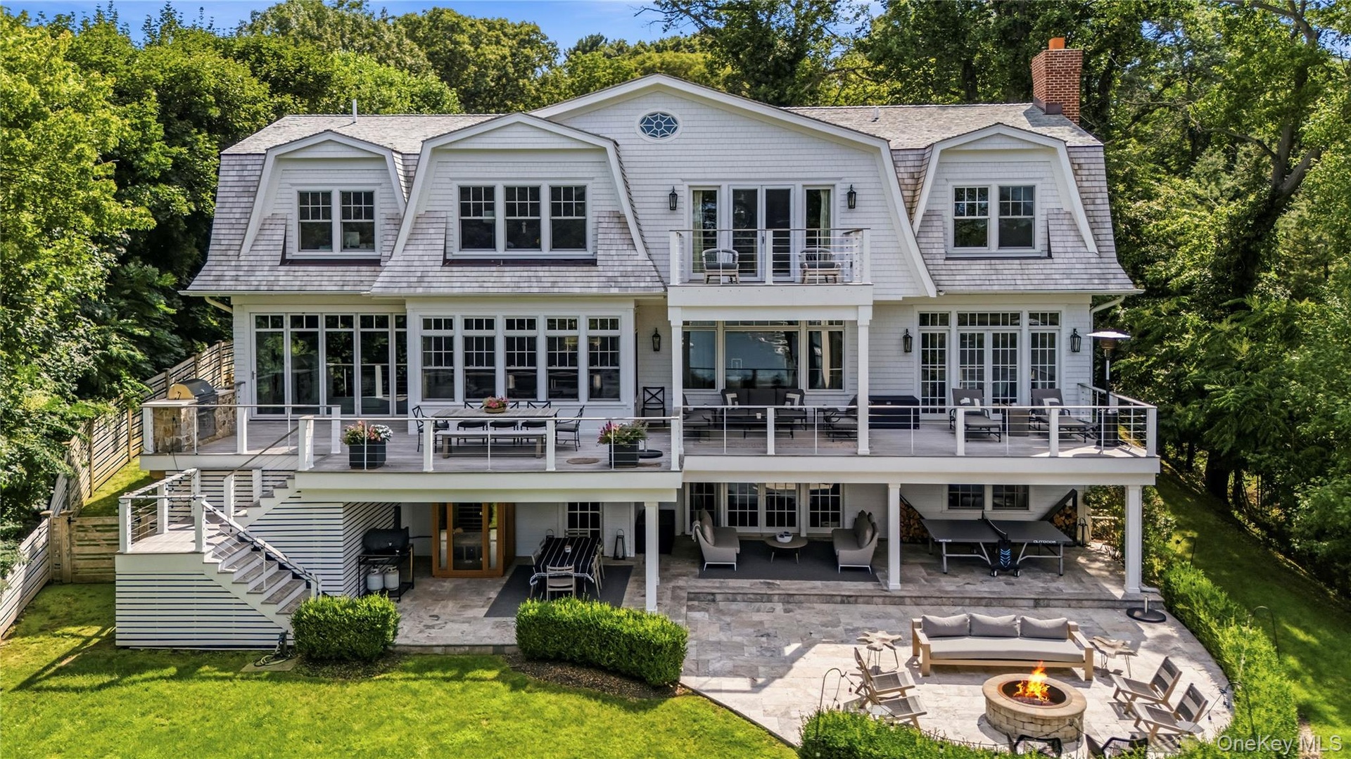 Multi-level exterior featuring dormer windows, a spacious deck with railing, an expansive lower level patio, and a fire pit