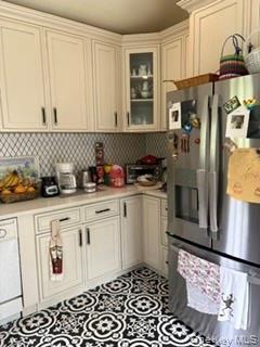 White cabinetry with crown molding, glass-front corner cabinet, stainless steel refrigerator, patterned floor tile, and light-toned countertops