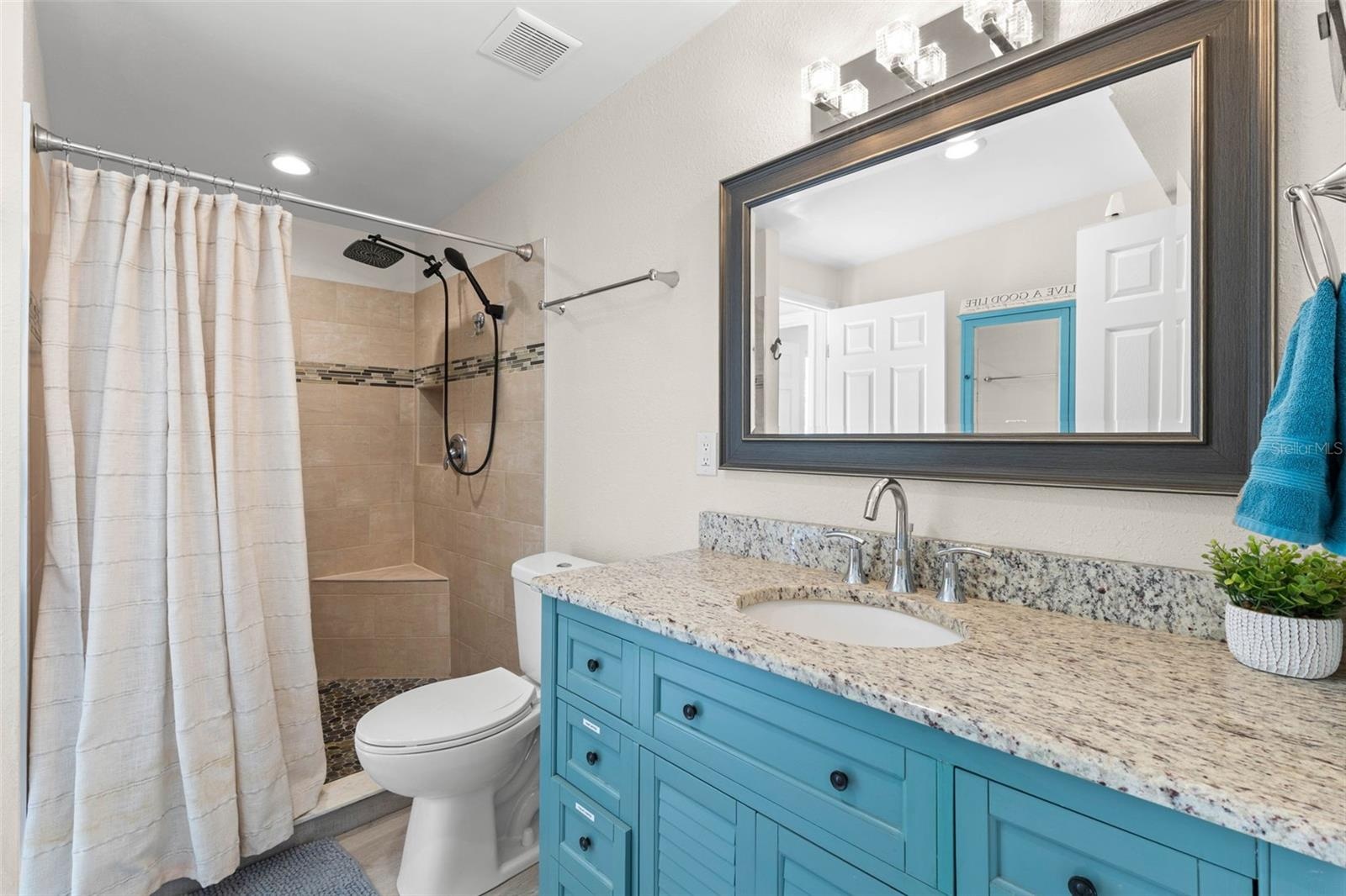The updated second bath features a turquoise vanity with granite countertop, framed mirror, modern lighting, and a tiled walk-in shower with built-in 