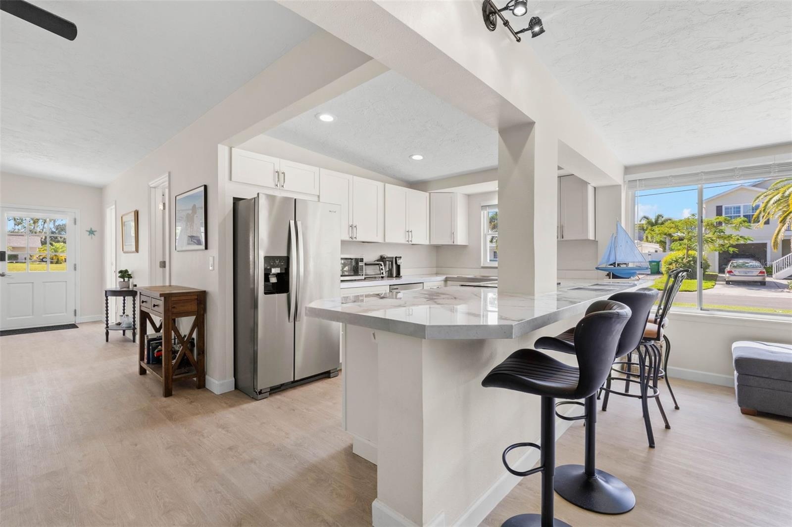 The updated kitchen (2025) pairs crisp white cabinetry and stainless steel appliances with expansive counter space and a wraparound breakfast bar that