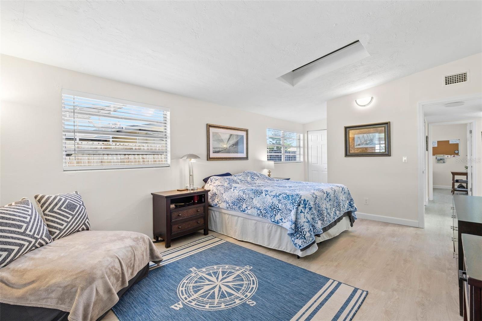 The spacious primary bedroom easily accommodates a king-size bed and a dedicated sitting area, with multiple windows, a skylight, neutral tones, and l