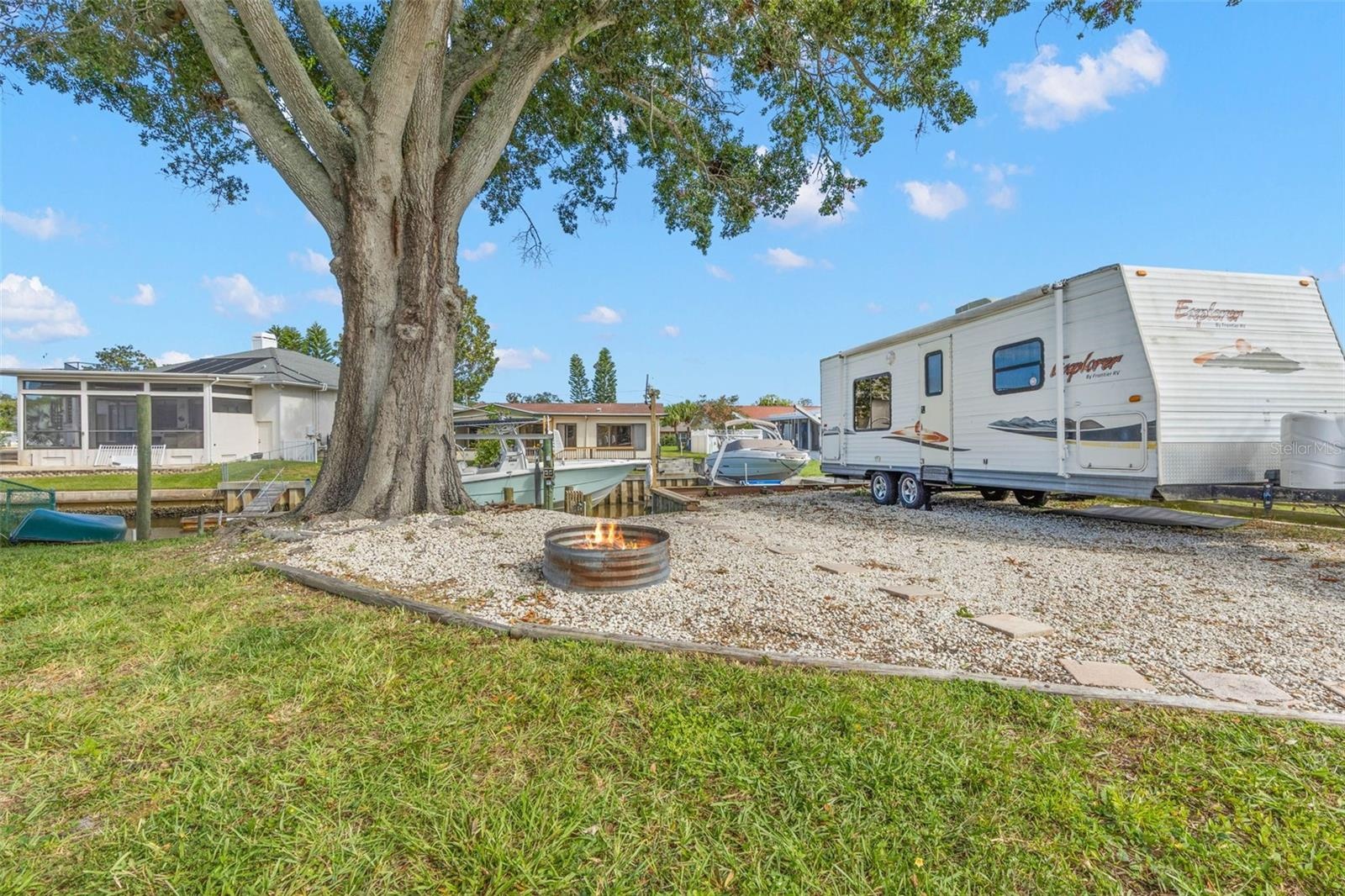 The extended side yard adds exceptional flexibility with room for RV, boat, or trailer parking, while a gravel gathering area with a fire pit sits ben