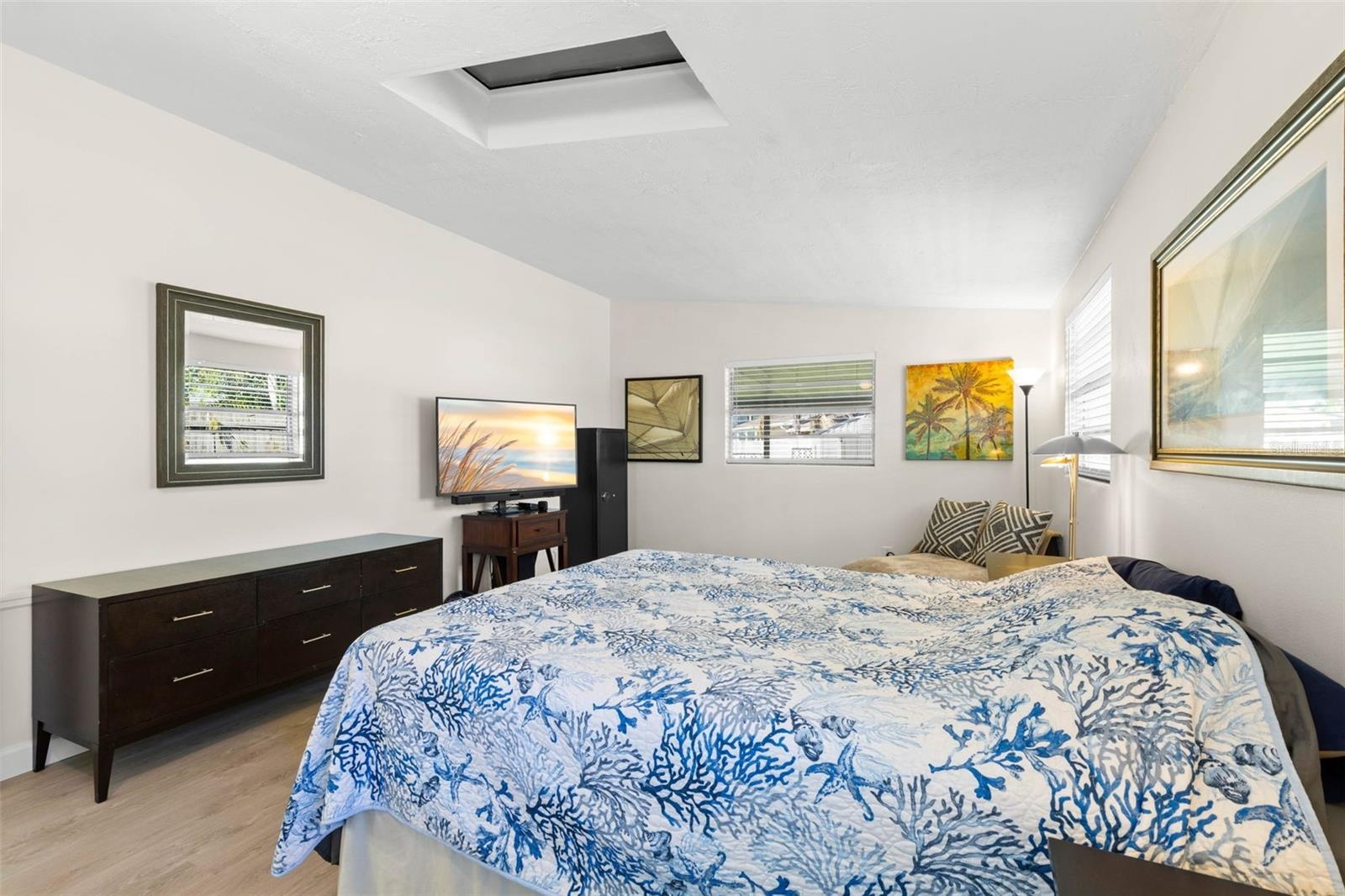 The primary bedroom offers exceptional space for both sleeping and lounging, with multiple windows, a skylight, neutral tones, and luxury vinyl plank 