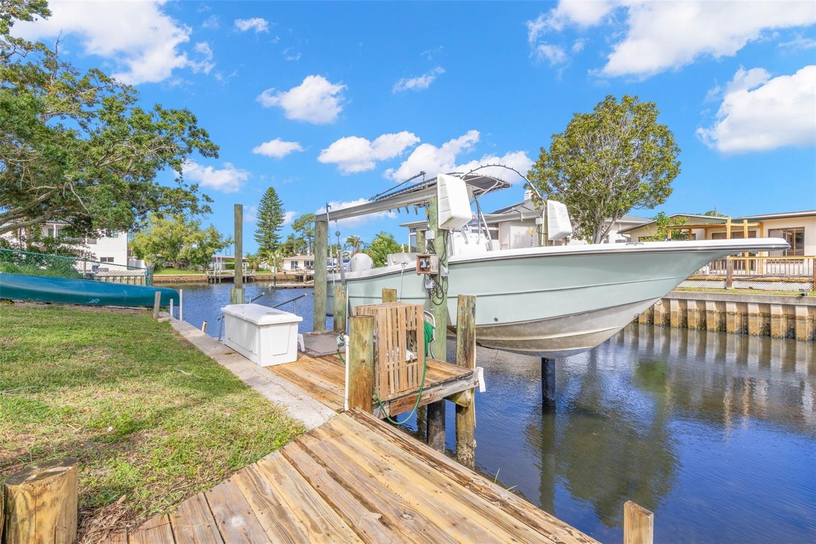 The waterfront setup is ready for serious boating, with a substantial wooden dock, 10,000-pound boat lift with davits, waterside storage, and a conven