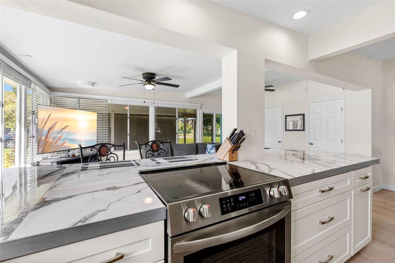 The updated kitchen (2025) showcases dramatic stone-look countertops, white Shaker-style cabinetry, stainless steel appliances, recessed lighting, and
