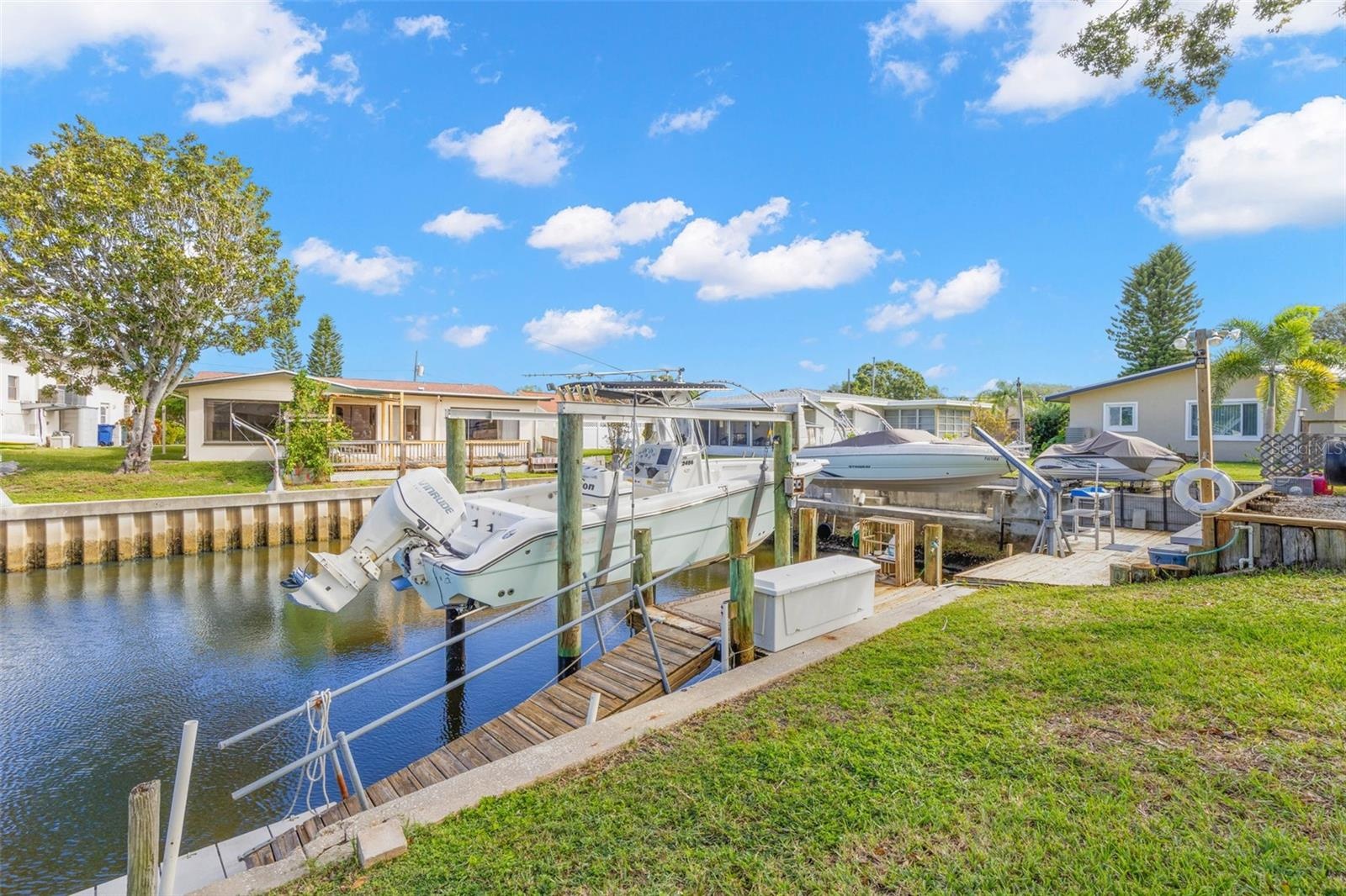 The canal frontage is equipped for easy days on the water, with a 10,000-pound boat lift, wooden dock, railed access walkway, waterside storage, and a