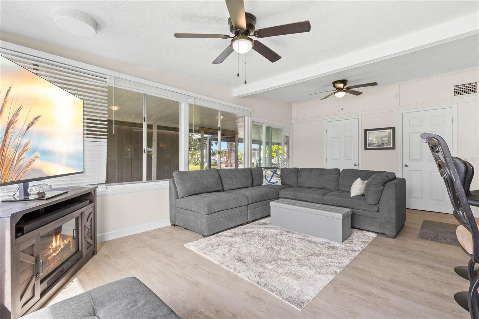 The spacious living room offers dual ceiling fans, luxury vinyl plank flooring, (2025) and a cozy fireplace, while a wall of windows and glass doors b