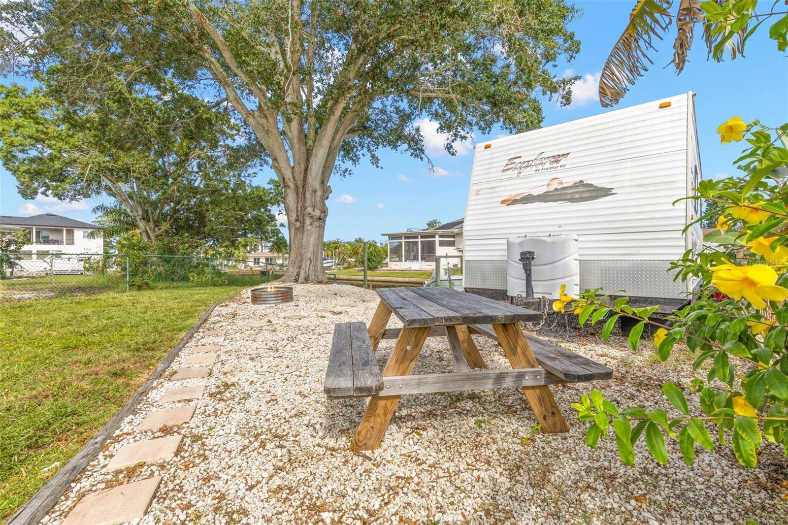 The oversized side yard offers dedicated space for RV, boat, or trailer parking, along with a gravel picnic area beneath a mature shade tree—another b