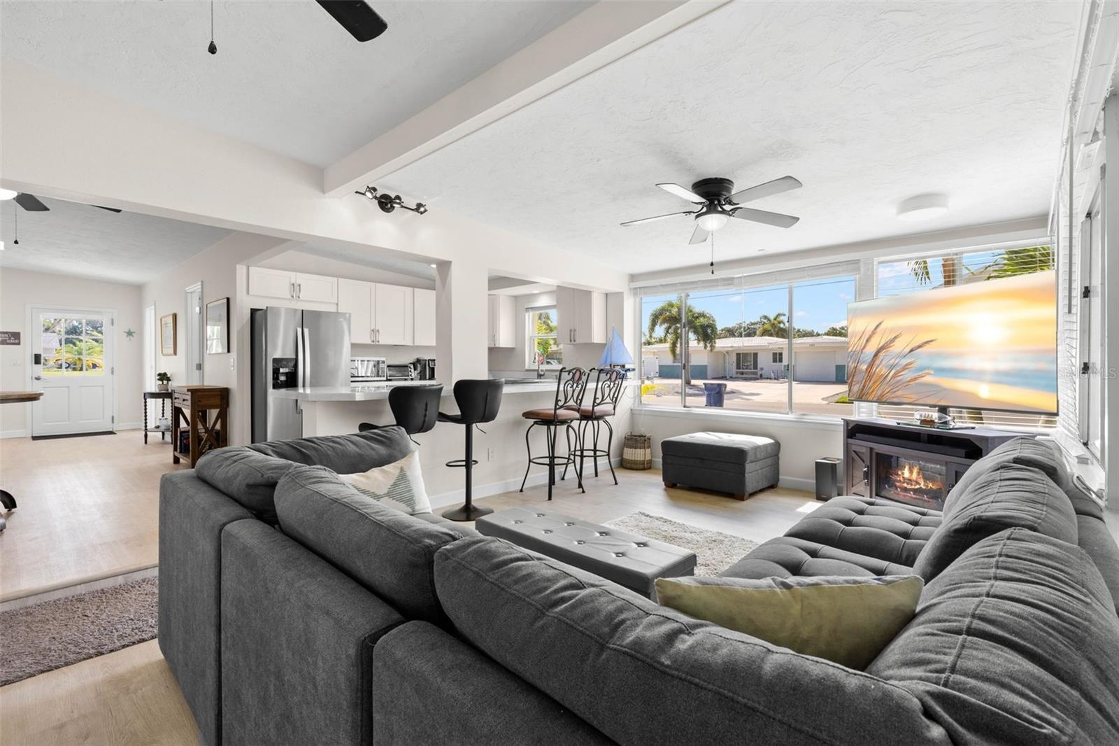 Expansive windows flood the living room with natural light, while the open connection to the updated kitchen, breakfast bar, ceiling fan, and fireplac