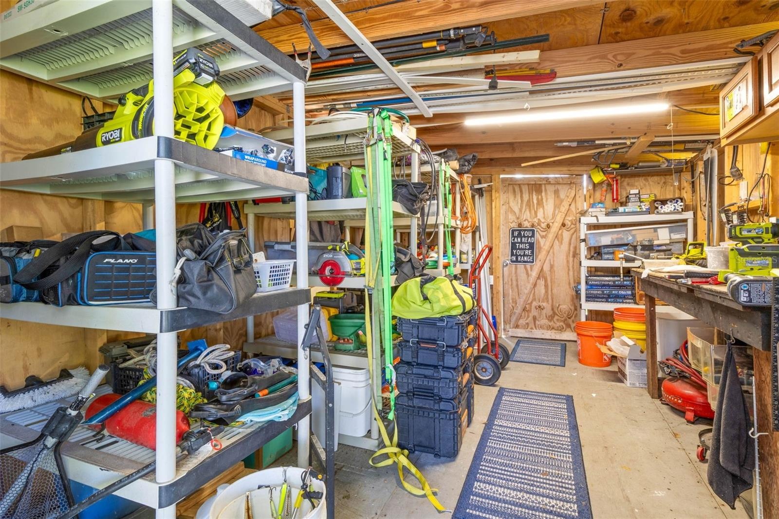 A dedicated workshop offers serious utility with abundant shelving, a long workbench, overhead storage, lighting, and plenty of room for tools, fishin