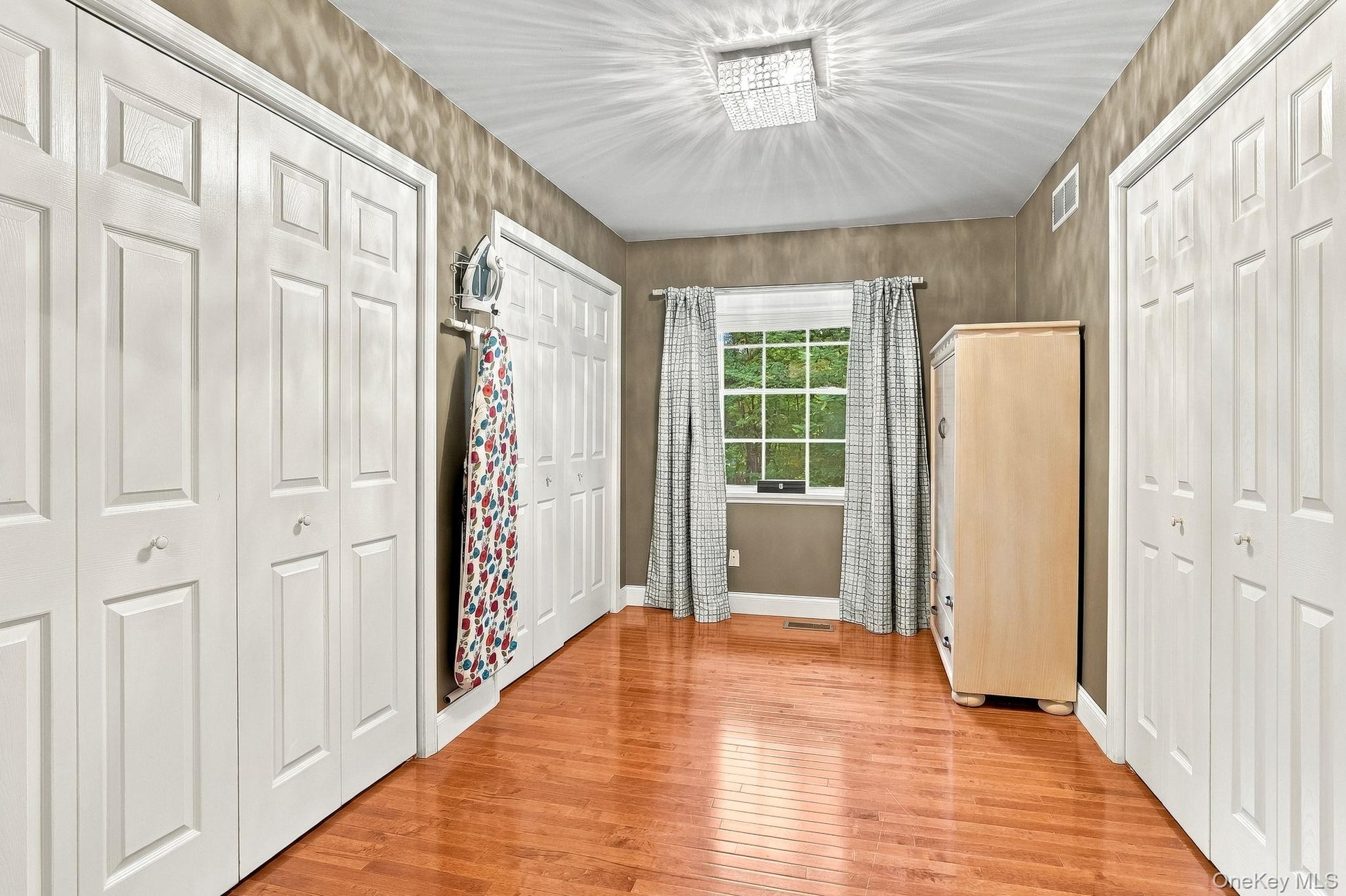 Hardwood-flooring, multiple paneled doors, single window, and a ceiling-mounted light fixture-Primary Closet