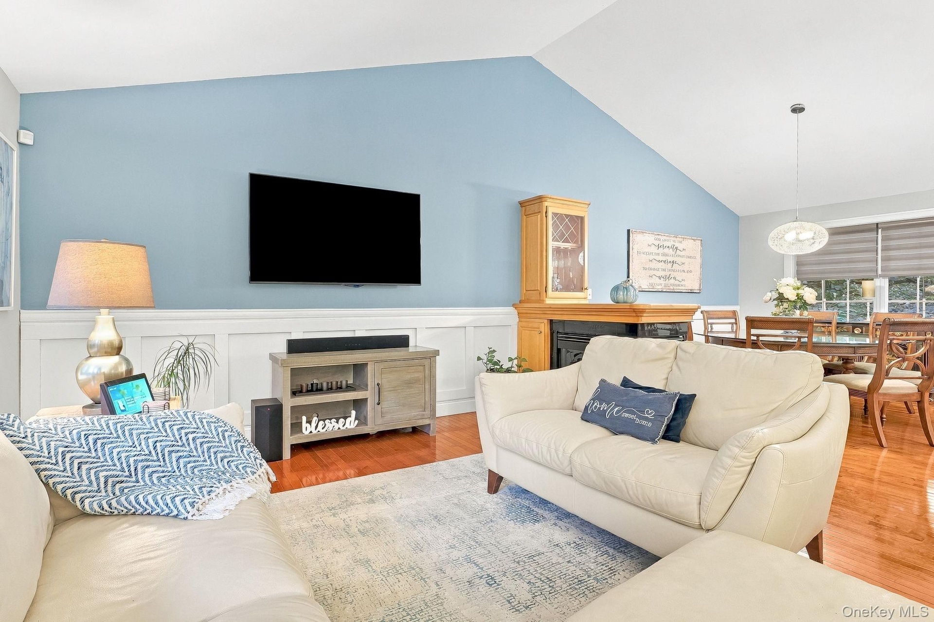 Vaulted ceiling, wood-flooring, wainscoting, fireplace with built-in cabinetry, and a modern dining pendant light