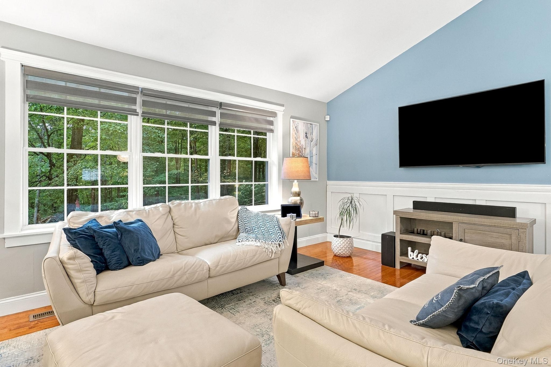Vaulted ceiling, hardwood flooring, large multi-pane windows, decorative wainscoting, and a wall-mounted display space