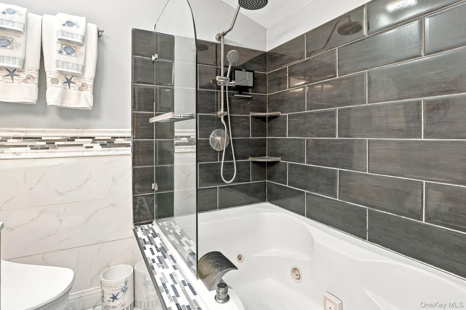 Bathtub with a glass shower panel, dark subway tile surround, integrated shelving, and a rain showerhead