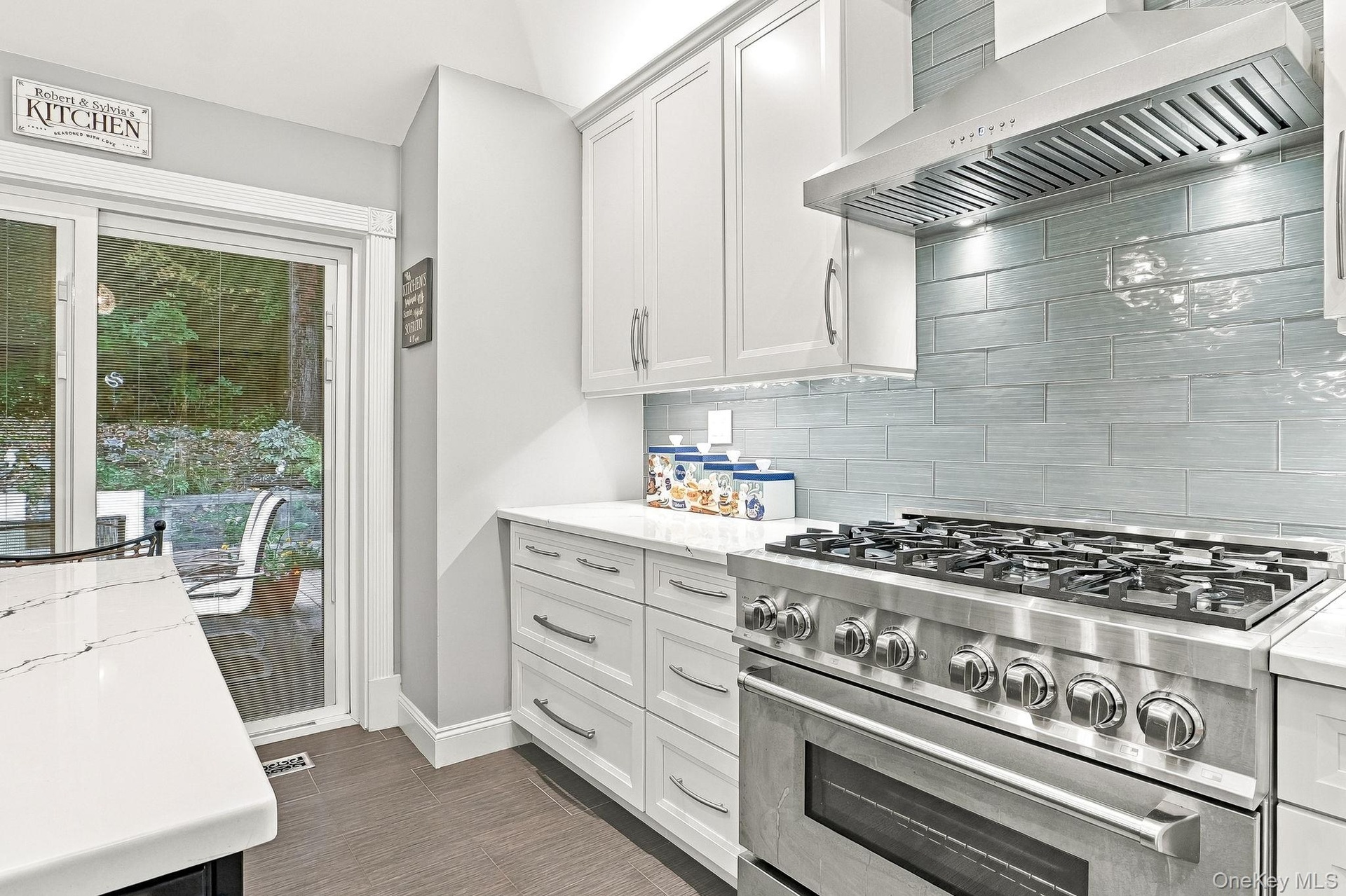 Stainless steel range with a ventilation hood, white cabinetry, tile backsplash, and light-toned countertops