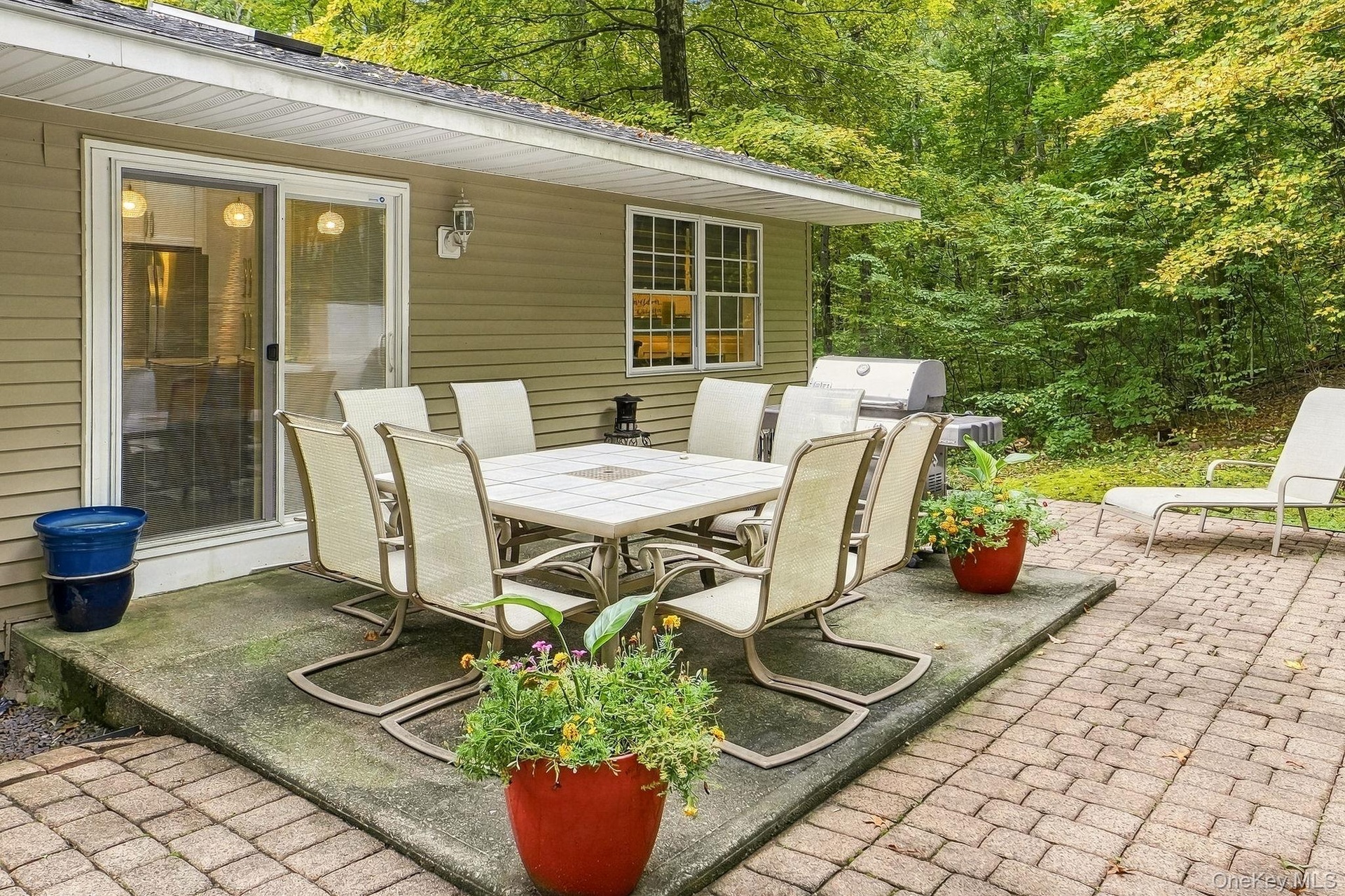 Patio area featuring a sliding glass door, a brick paver section, and mature trees in the background