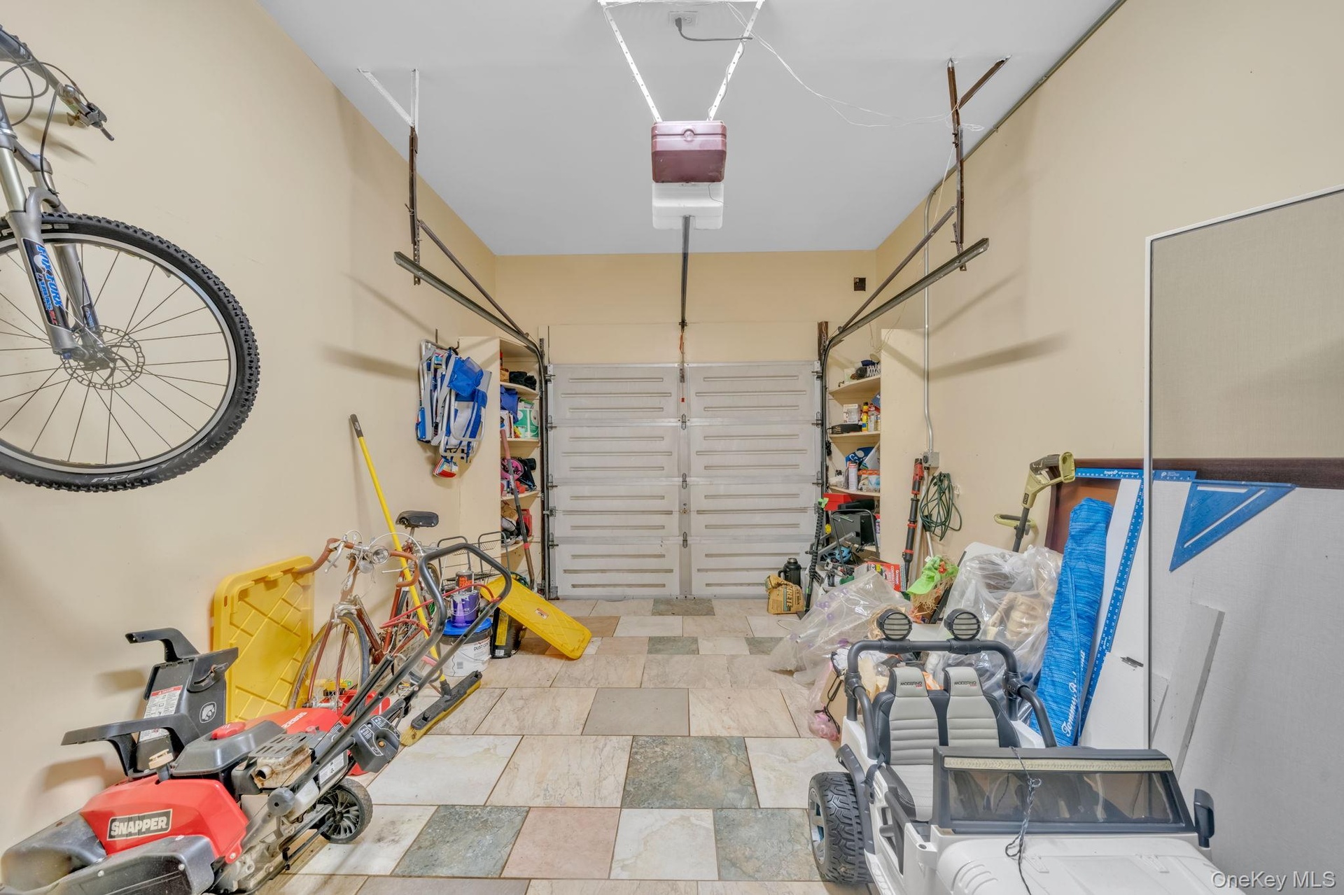 Garage space featuring multi-toned tile flooring, light-toned walls, and a built-in storage rack