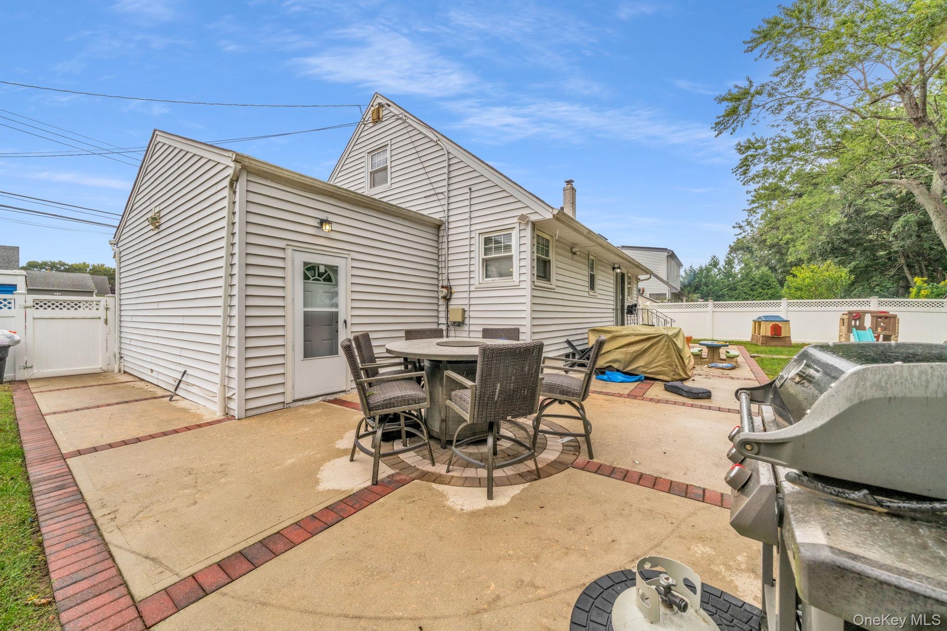 Spacious rear patio with concrete and brick accents, white vinyl siding, rear door with decorative glass, and a white fence