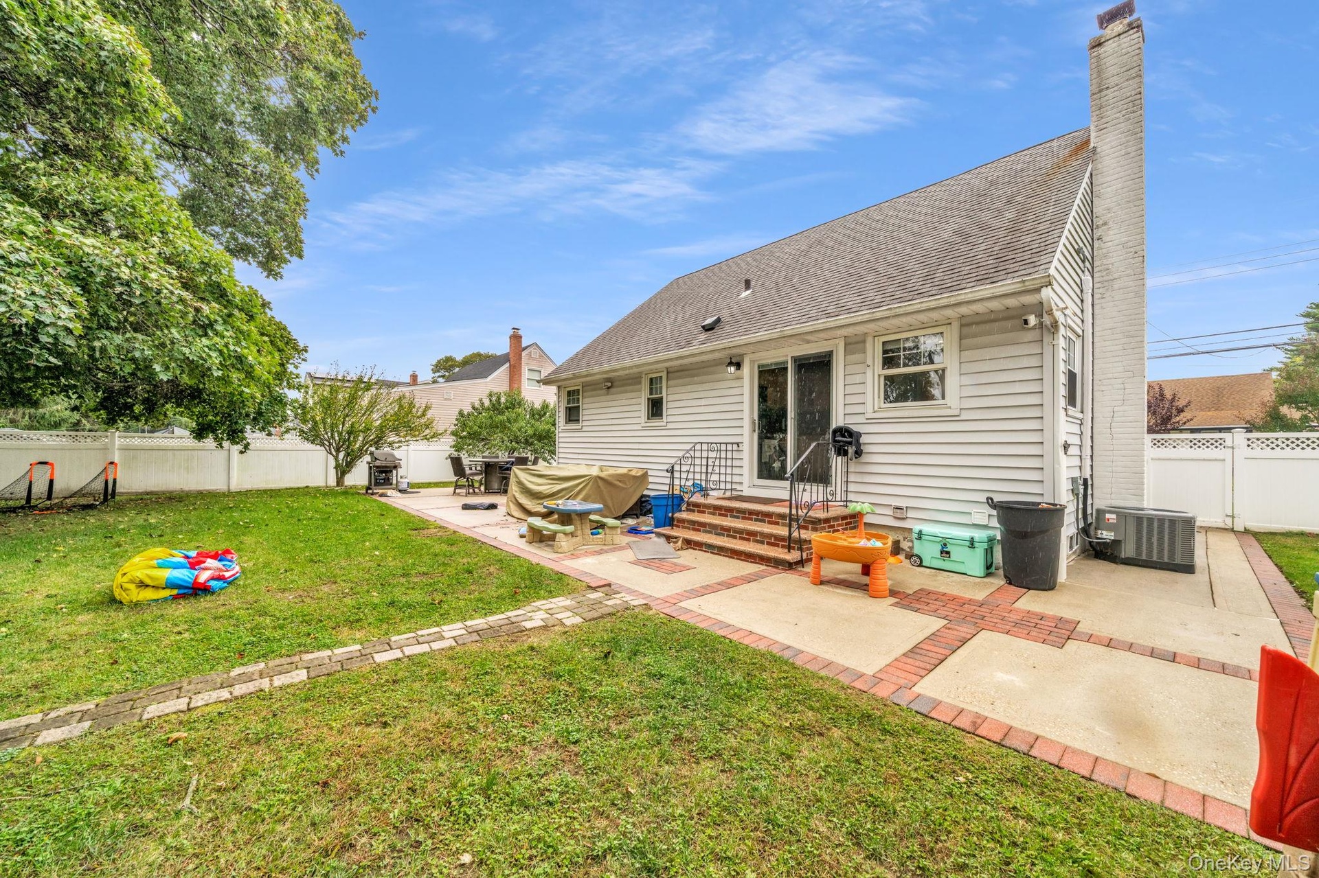 Expansive backyard featuring a manicured lawn, white privacy fencing, a brick and concrete patio.