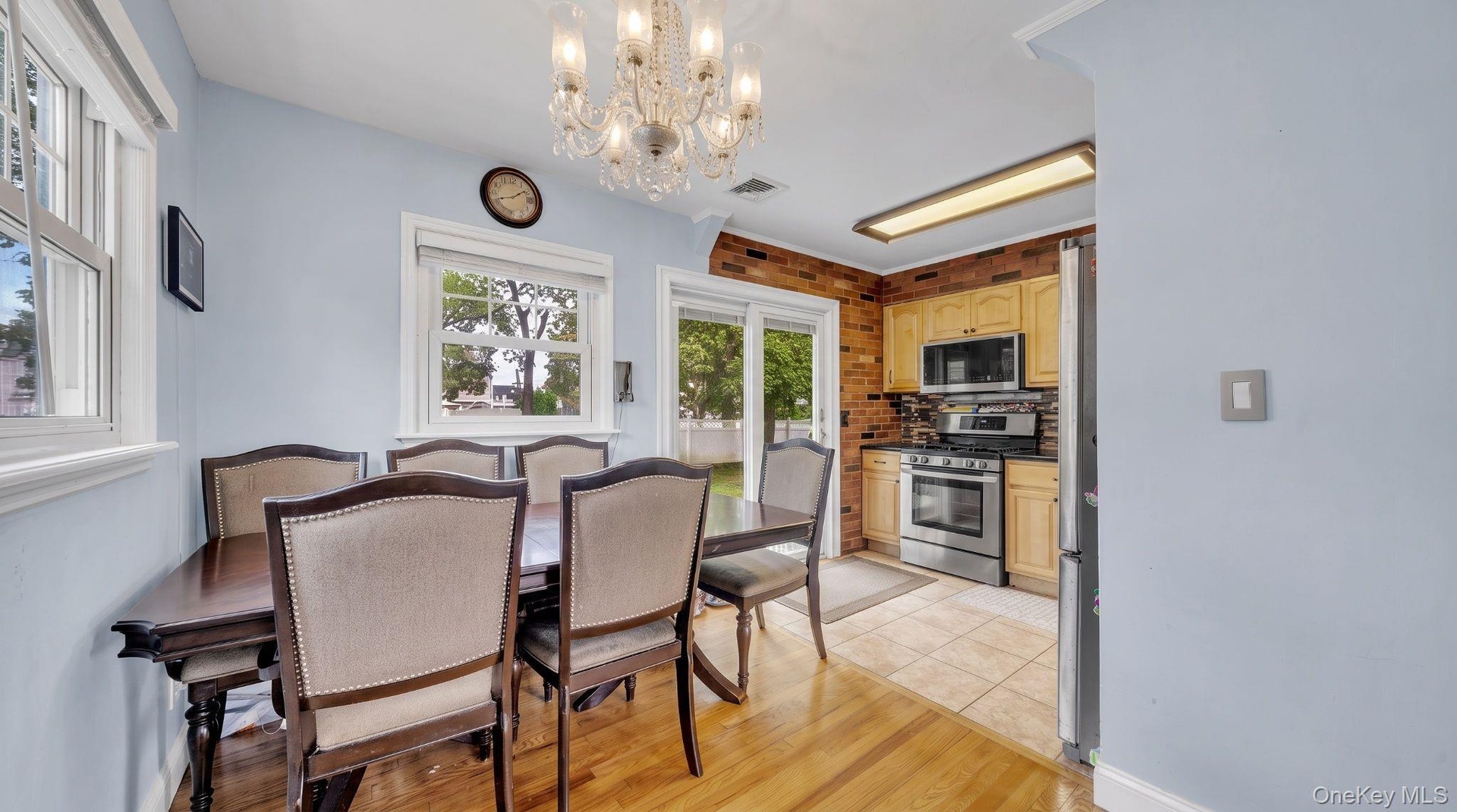 Wood-finish flooring, multiple windows, kitchen with stainless steel appliances, brick-finish kitchen wall, sliding glass patio door