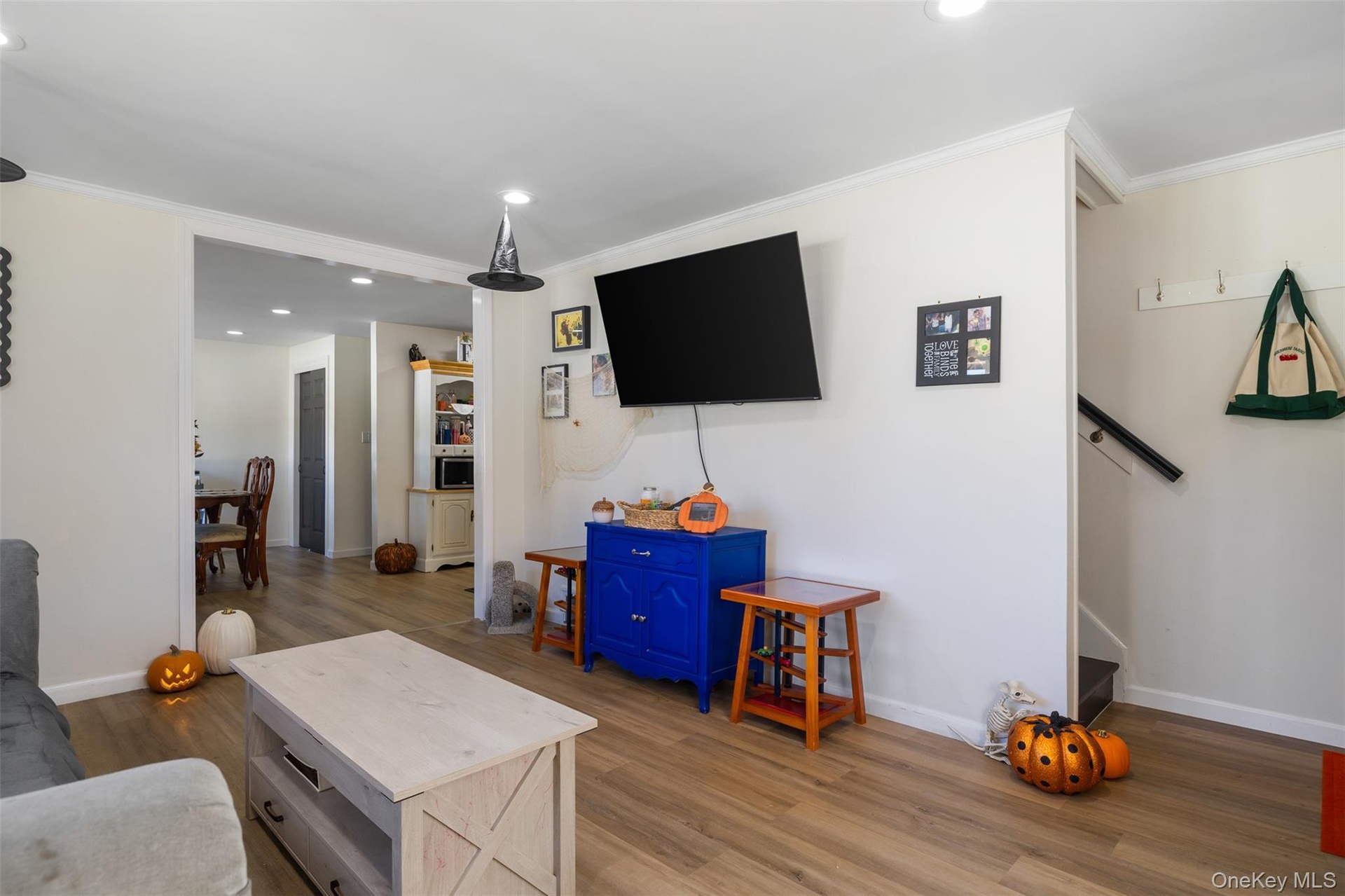 Wood-finish flooring throughout, recessed ceiling lighting, crown molding, and an open entryway to an additional room