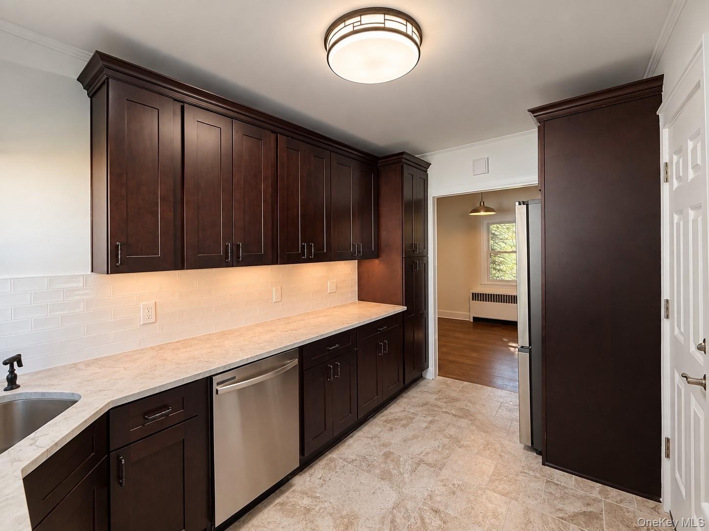 Dark wood cabinetry with crown molding, light-toned countertop, stainless steel dishwasher, tile flooring, and white subway tile backsplash