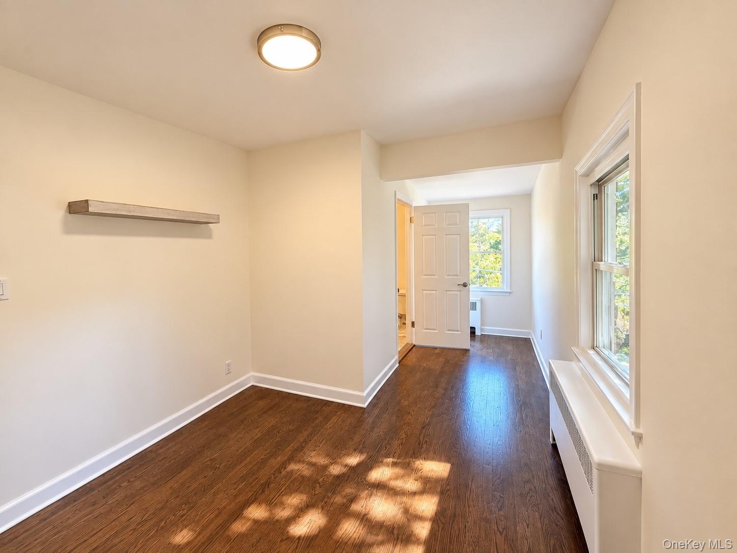 Wood-finish flooring, white trim, recessed lighting, white panel door, and window with natural light, door to a full bathroom.