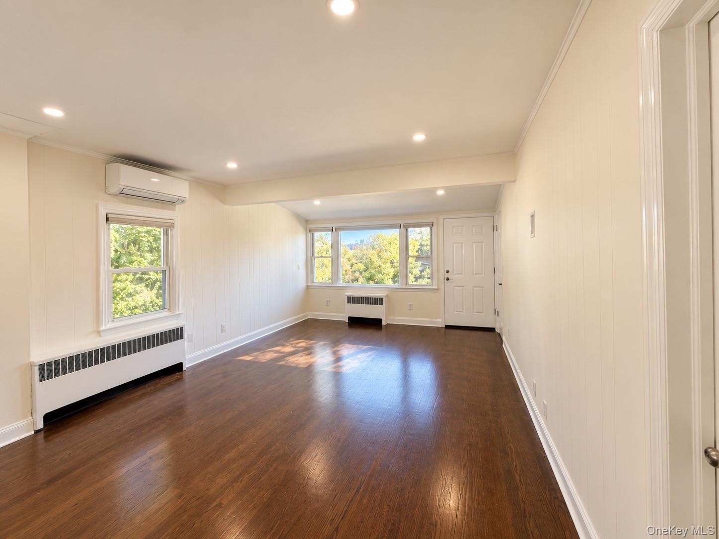 Wood-finish flooring throughout, recessed lighting, white paneled walls, multiple windows, and a split-system air conditioning unit
