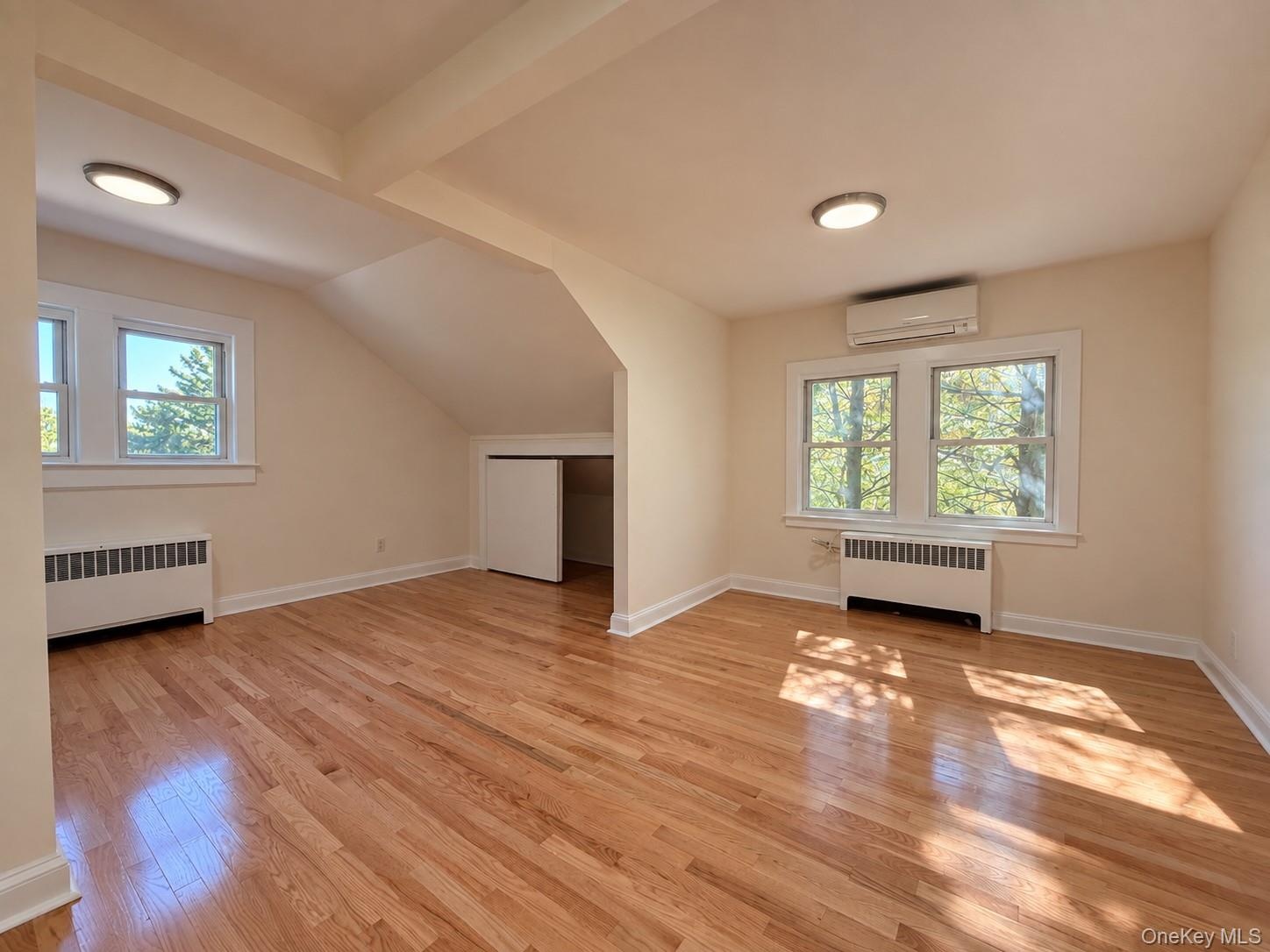 Hardwood flooring, multiple windows, built-in air conditioning unit, ceiling-mounted lighting, and a closet with bifold doors