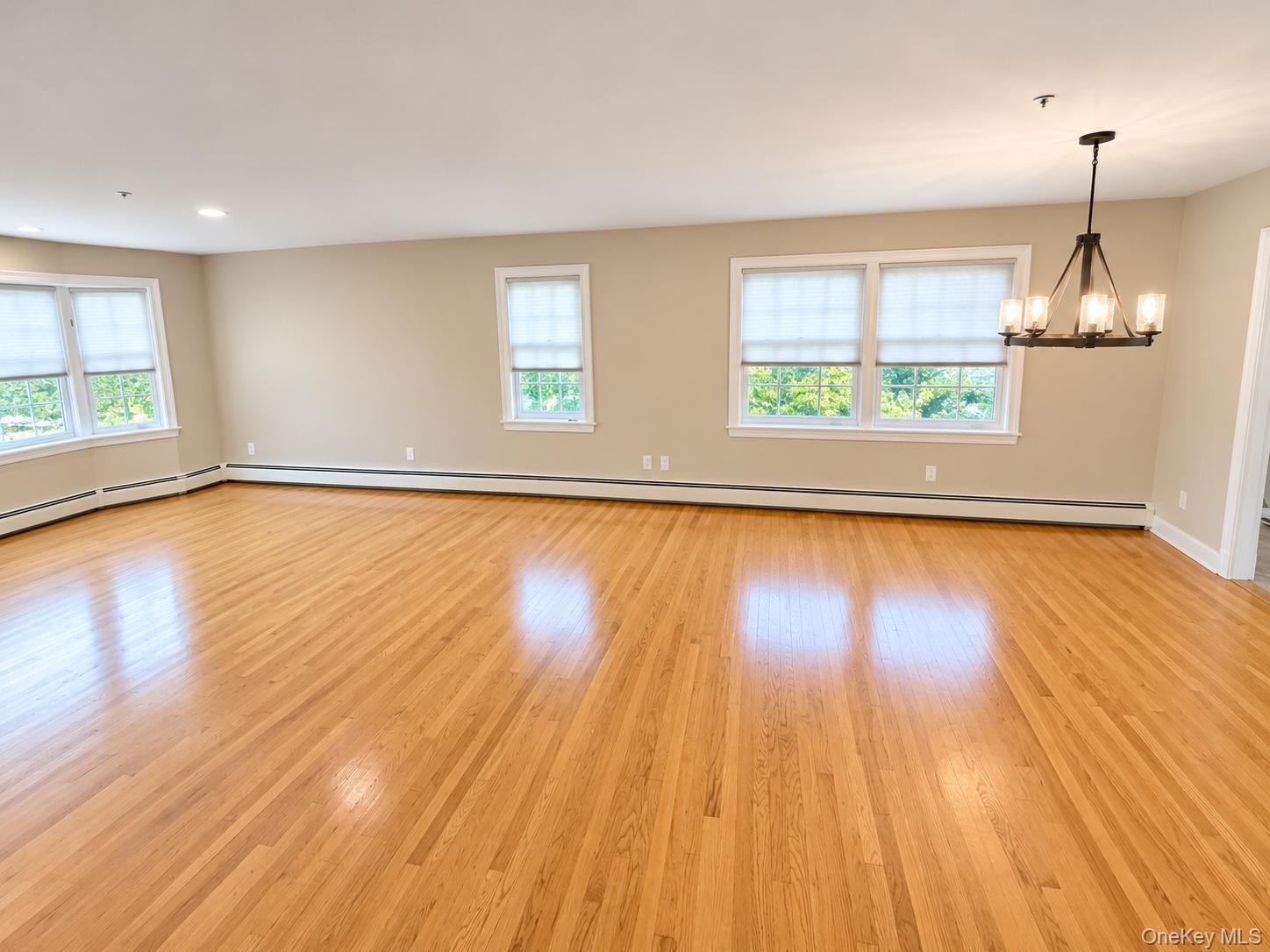 Combined living room and dining room with hardwood flooring and chandelier.