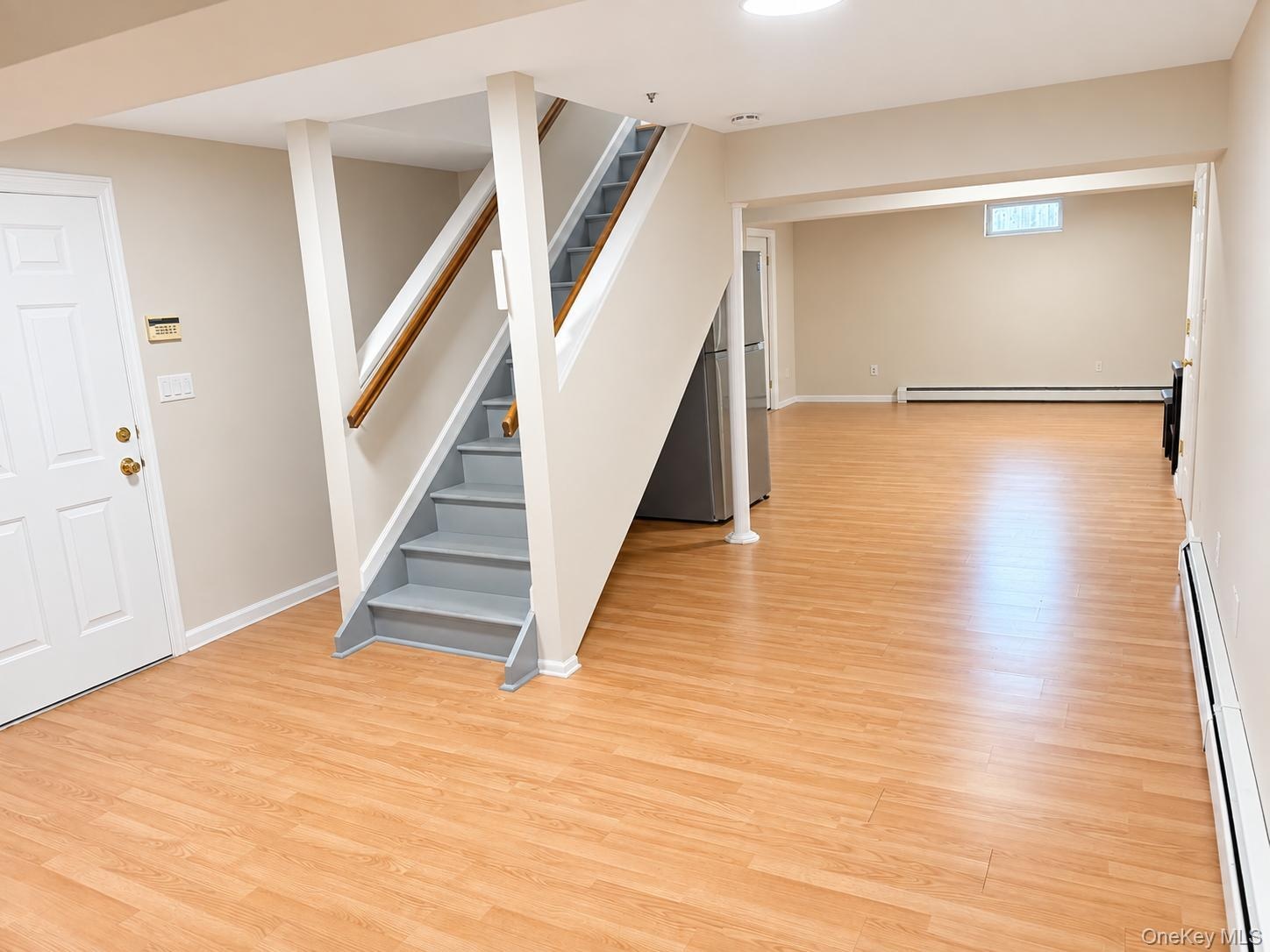 Expansive lower level with wood-finish flooring, a full staircase with wood handrail, and white paneled door