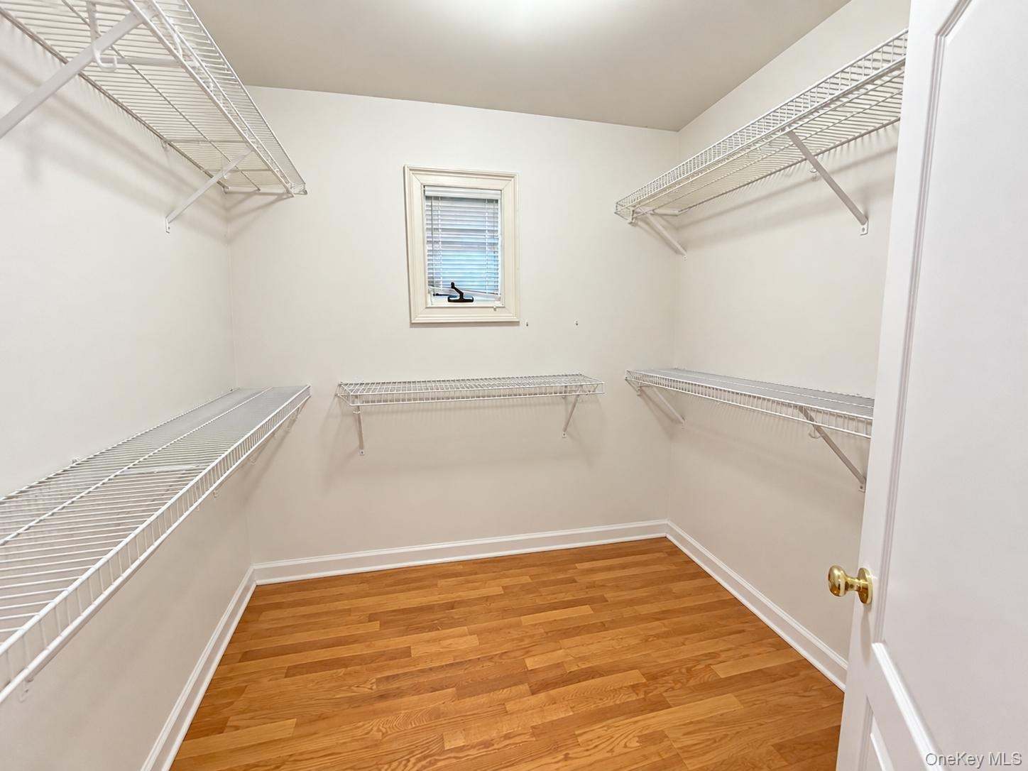 Walk-in closet with wire shelving, wood-finish flooring, and a window for natural light