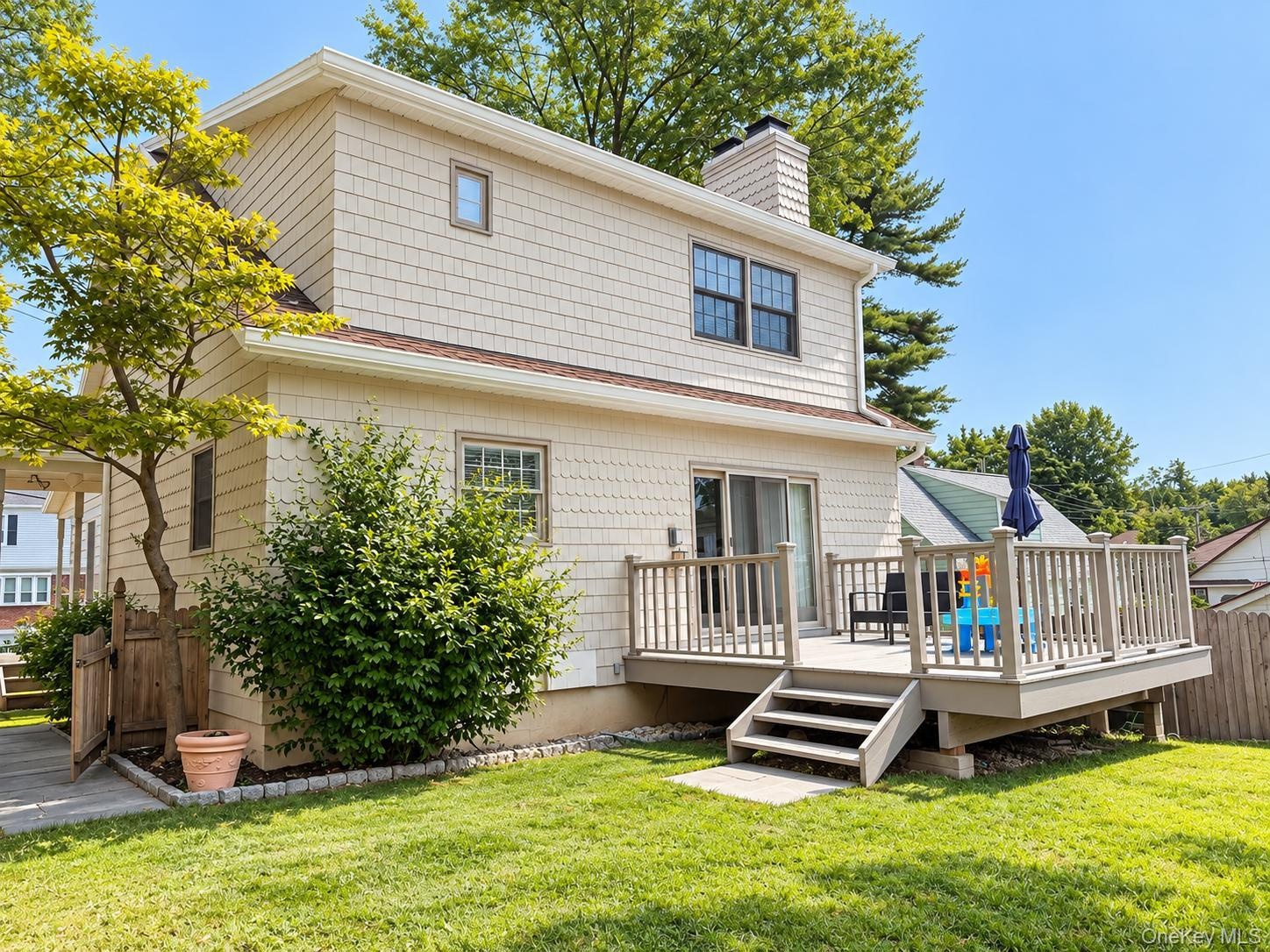 Two-story residence with shake siding, featuring a substantial outdoor deck with railing, sliding glass door access, and a wood privacy fence