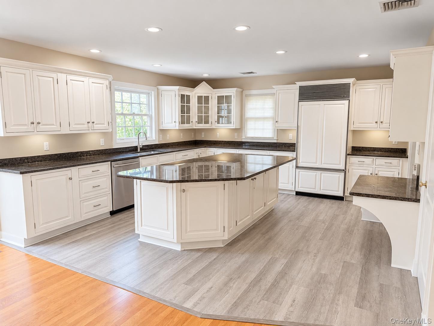 Expansive kitchen featuring white cabinetry, dark stone countertops, a large center island, and integrated stainless steel appliances