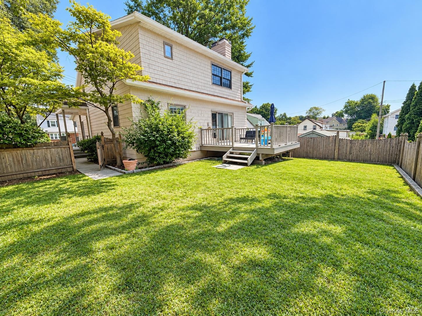 Expansive lawn area with a wood deck, wood privacy fencing, and mature landscaping