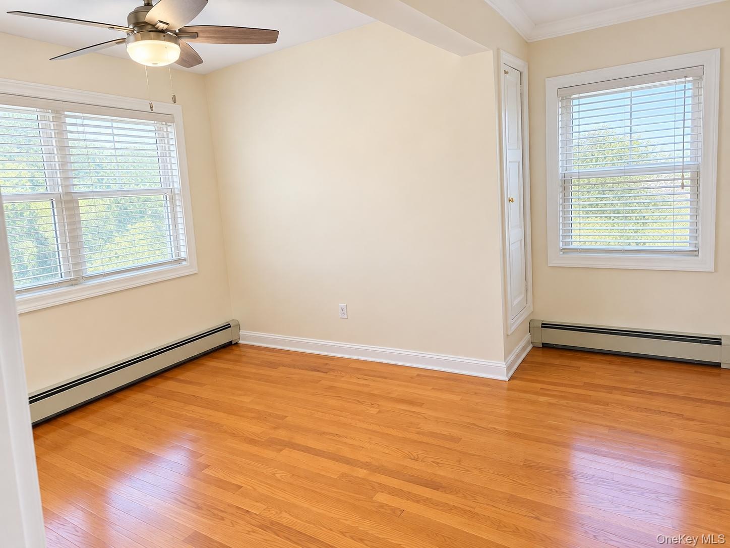 Hardwood flooring, two windows with blinds, ceiling fan, and built-in vertical cabinetry