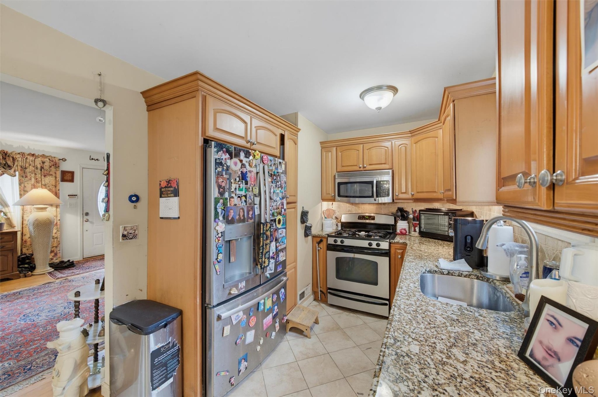 Kitchen featuring light wood cabinetry, stainless steel appliances, granite countertops, and tile flooring
