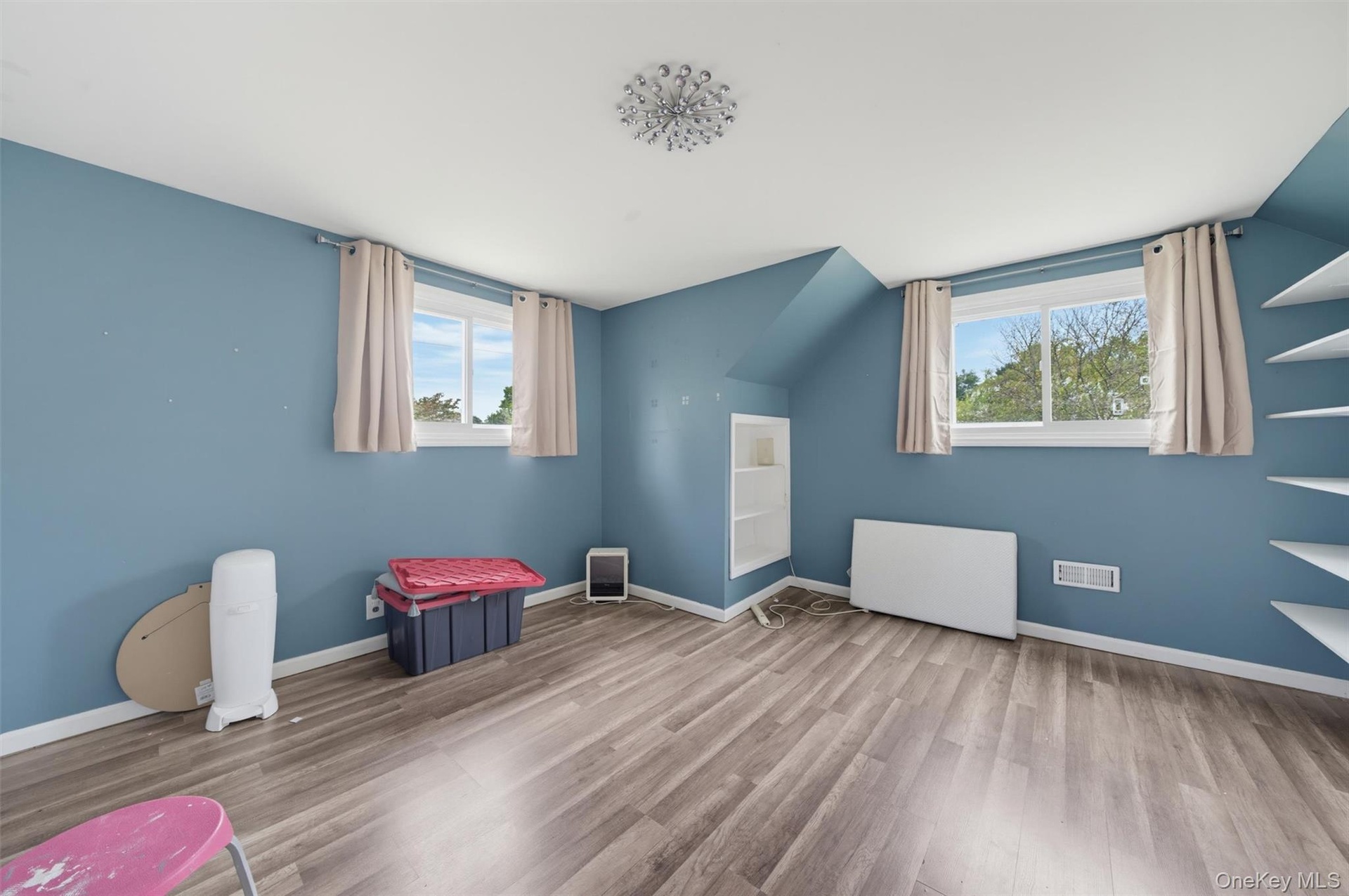 Sloped ceiling room featuring wood-finish flooring, recessed shelving, built-in wall shelving, dual windows, and a flush-mount ceiling light fixture