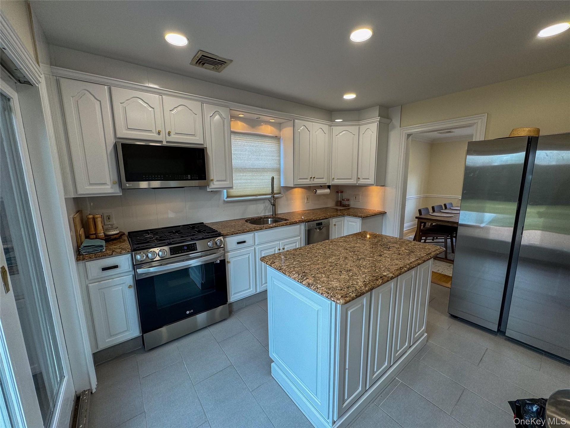 Kitchen featuring white cabinetry, granite countertops, stainless steel appliances, a center island, and tile flooring