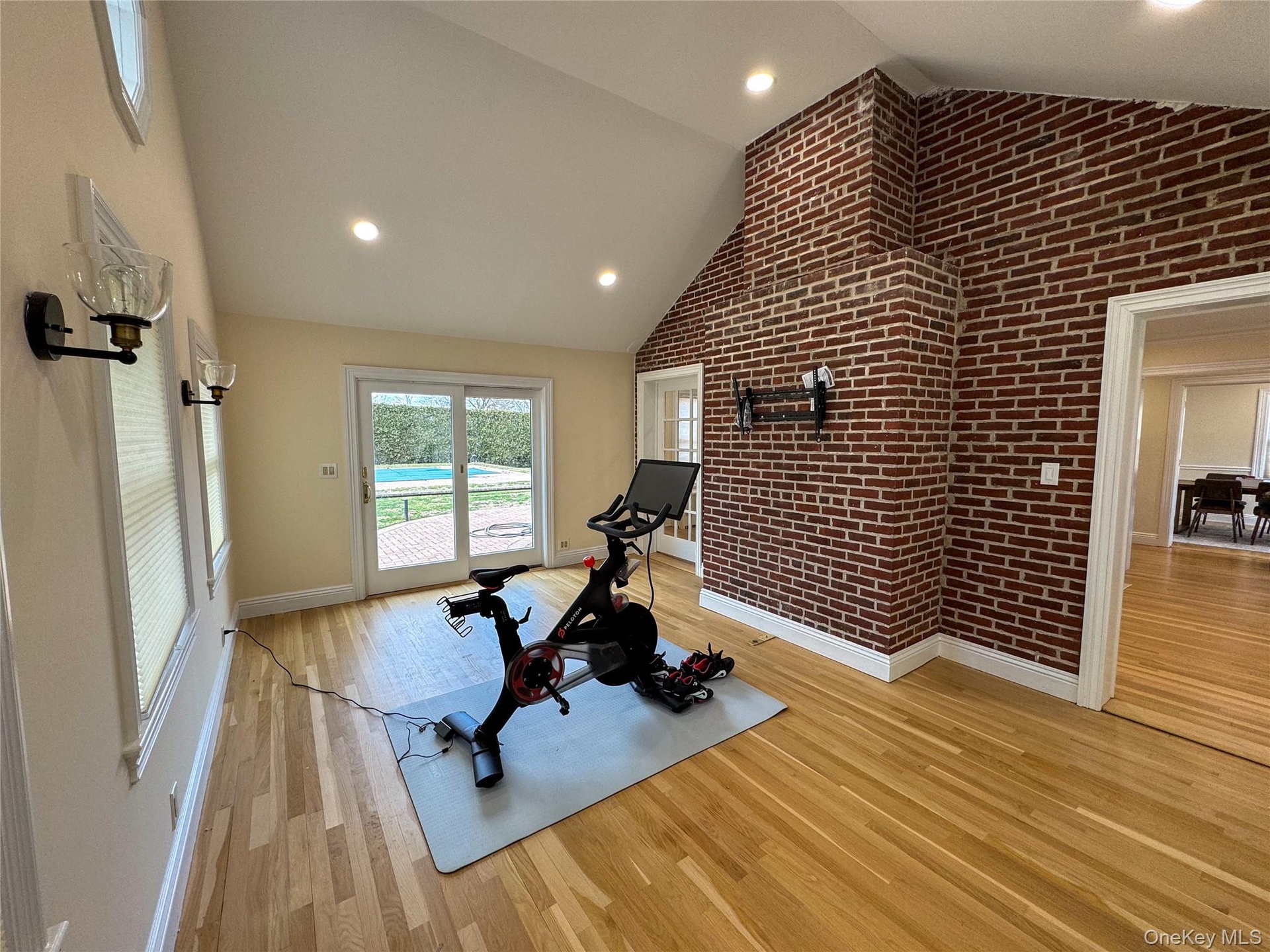 Vaulted ceiling with recessed lighting, exposed brick wall, light wood-finish flooring, sliding glass doors, and wall sconces