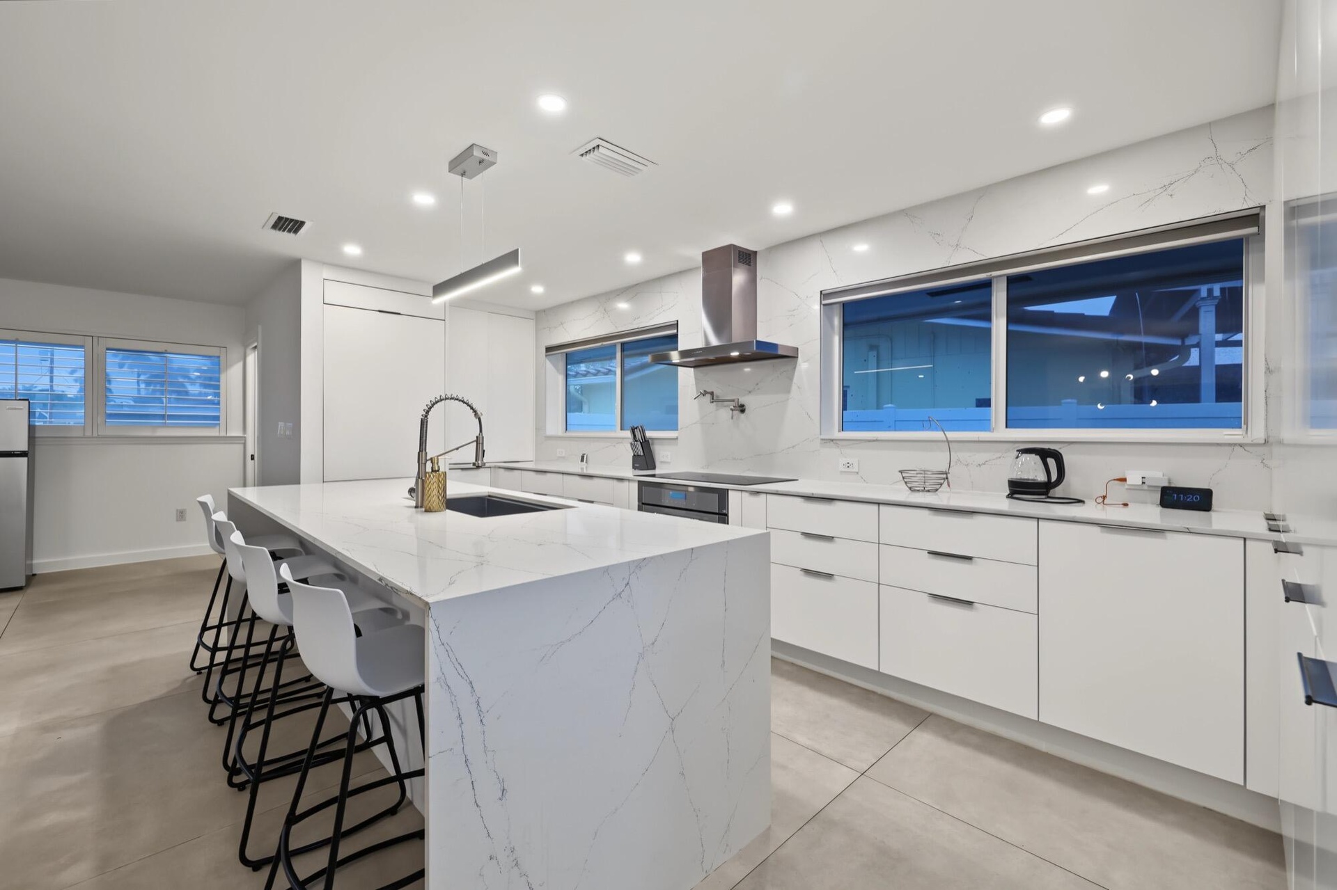 Spacious kitchen featuring a waterfall island, white flat-panel cabinetry, integrated stainless steel appliances, a stainless steel range hood, and re