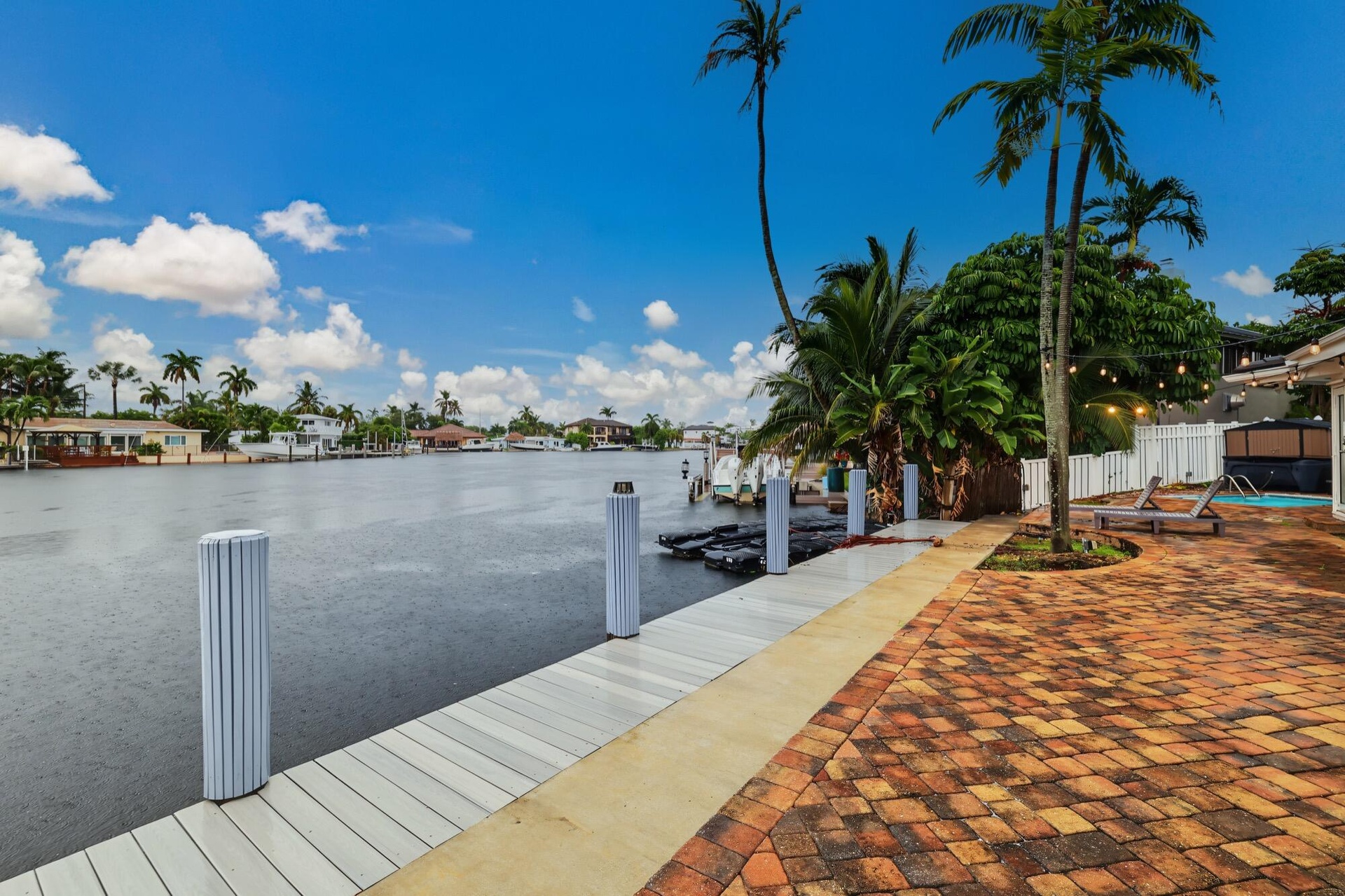 Waterfront property featuring a private dock, brick paver patio, lush tropical landscaping, and a pool with an attached spa