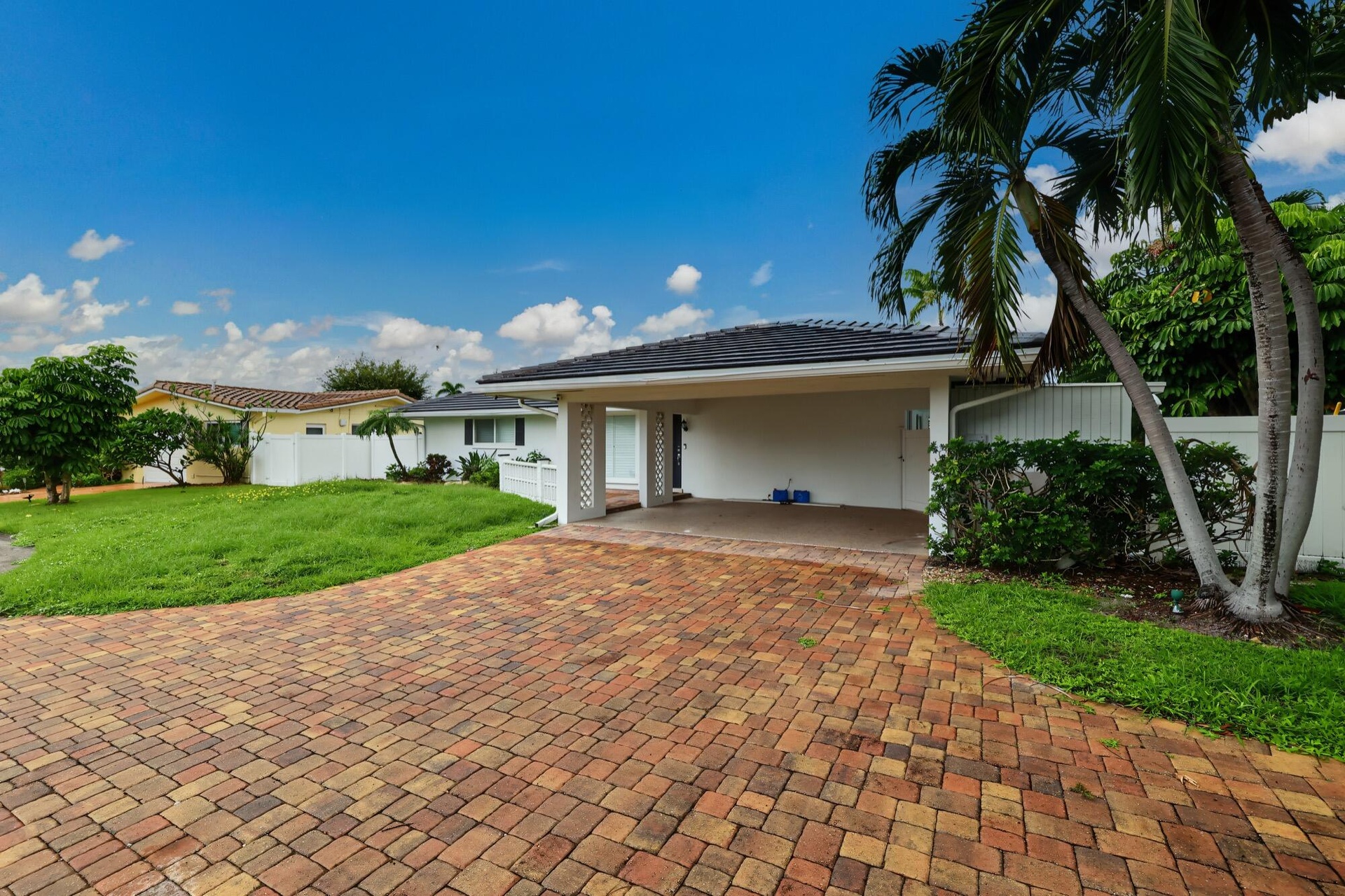 Paved driveway with multi-tone brick pavers, carport, and lush tropical landscaping