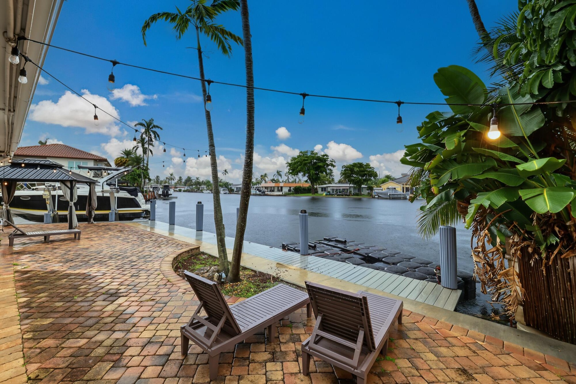 Waterfront property featuring a brick paver patio, mature palm trees, and a private dock