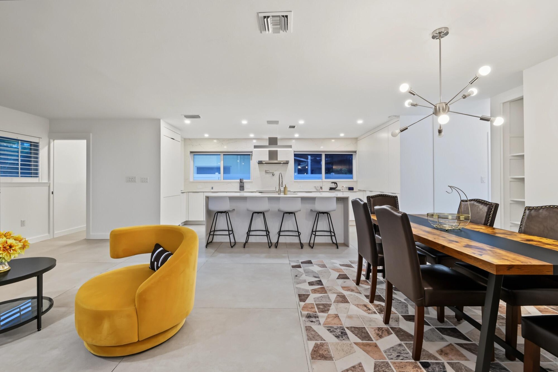 Open-concept living space featuring a modern kitchen with an island, a dining area with a contemporary chandelier, and light-toned flooring throughout