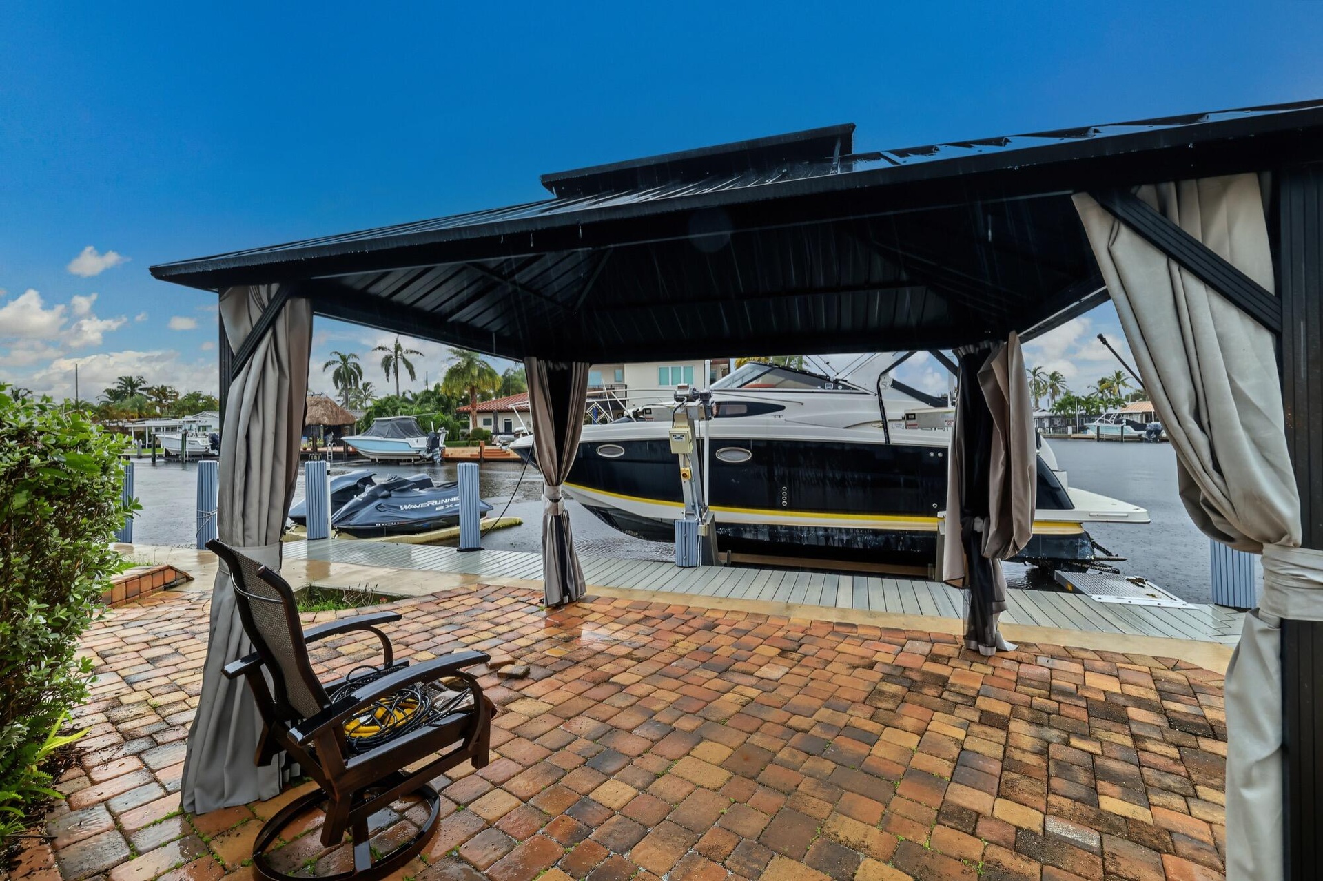 Brick paver patio featuring a black metal gazebo with retractable privacy curtains and a waterfront dock with boat access