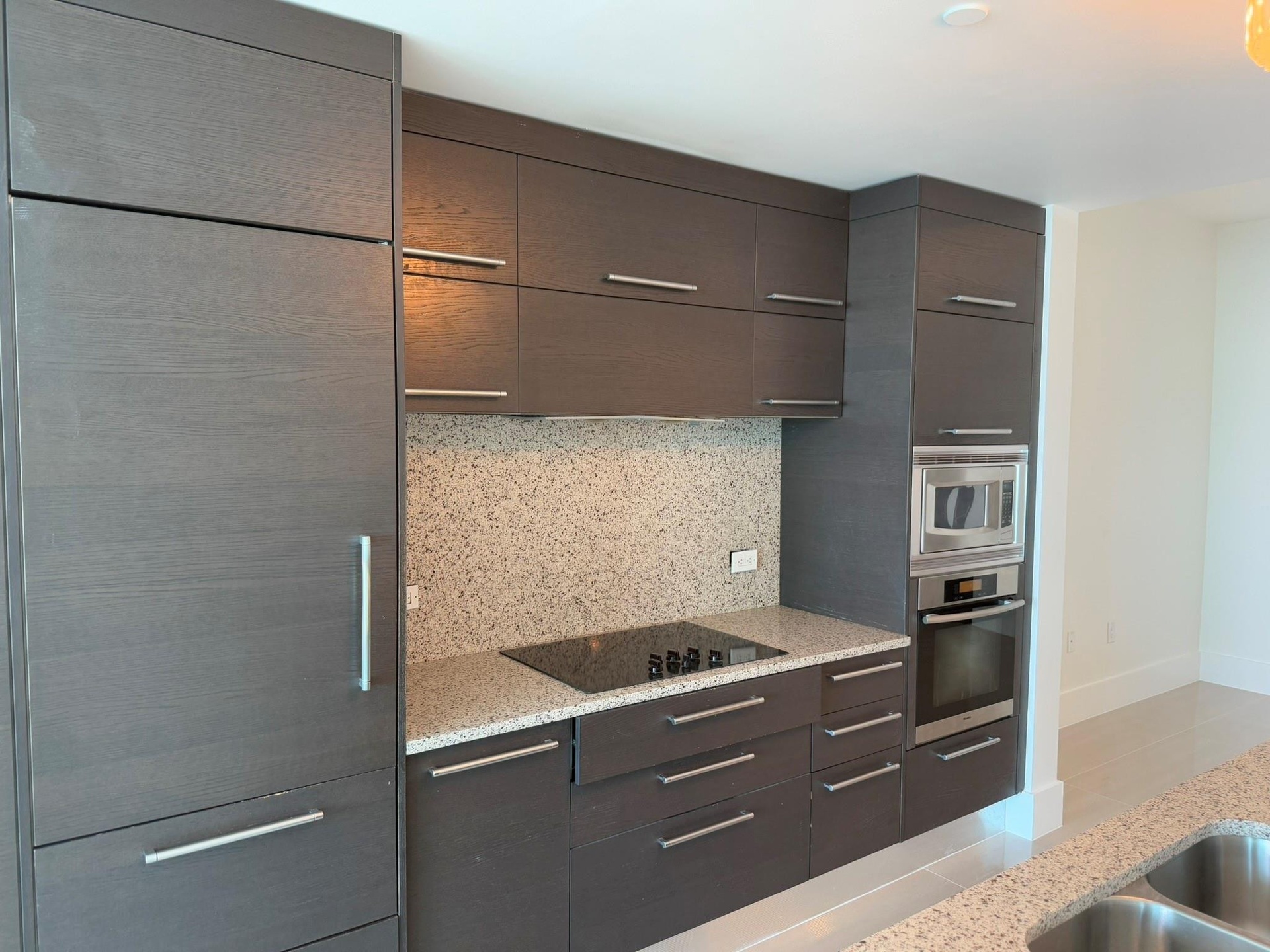 Contemporary kitchen featuring integrated paneled refrigeration, dark wood-finish cabinetry, speckled countertops, and a built-in oven and microwave
