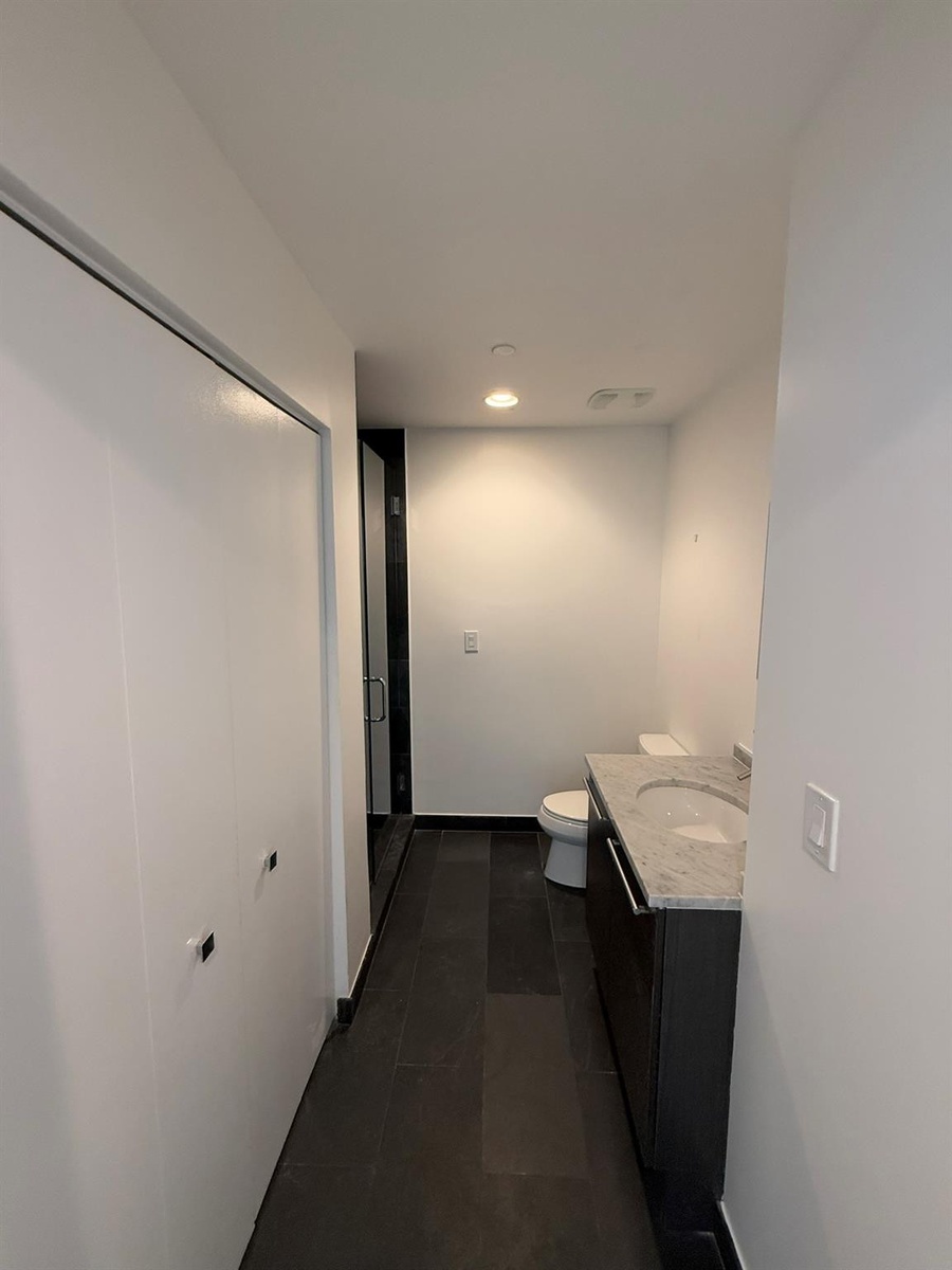 Bathroom featuring dark tile flooring, a single vanity with a light-toned countertop and integrated sink, a toilet, and white walls