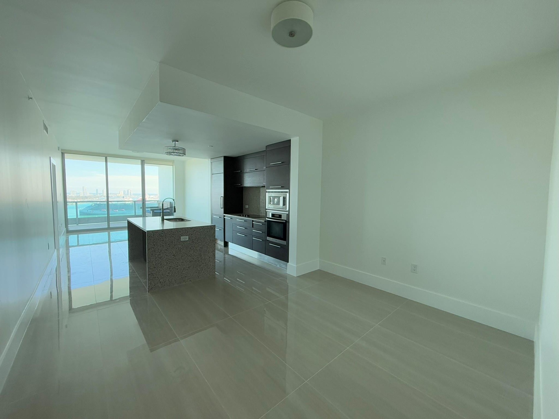 Open-concept living area featuring large format tile flooring, floor-to-ceiling windows, and a modern kitchen with dark cabinetry, integrated applianc