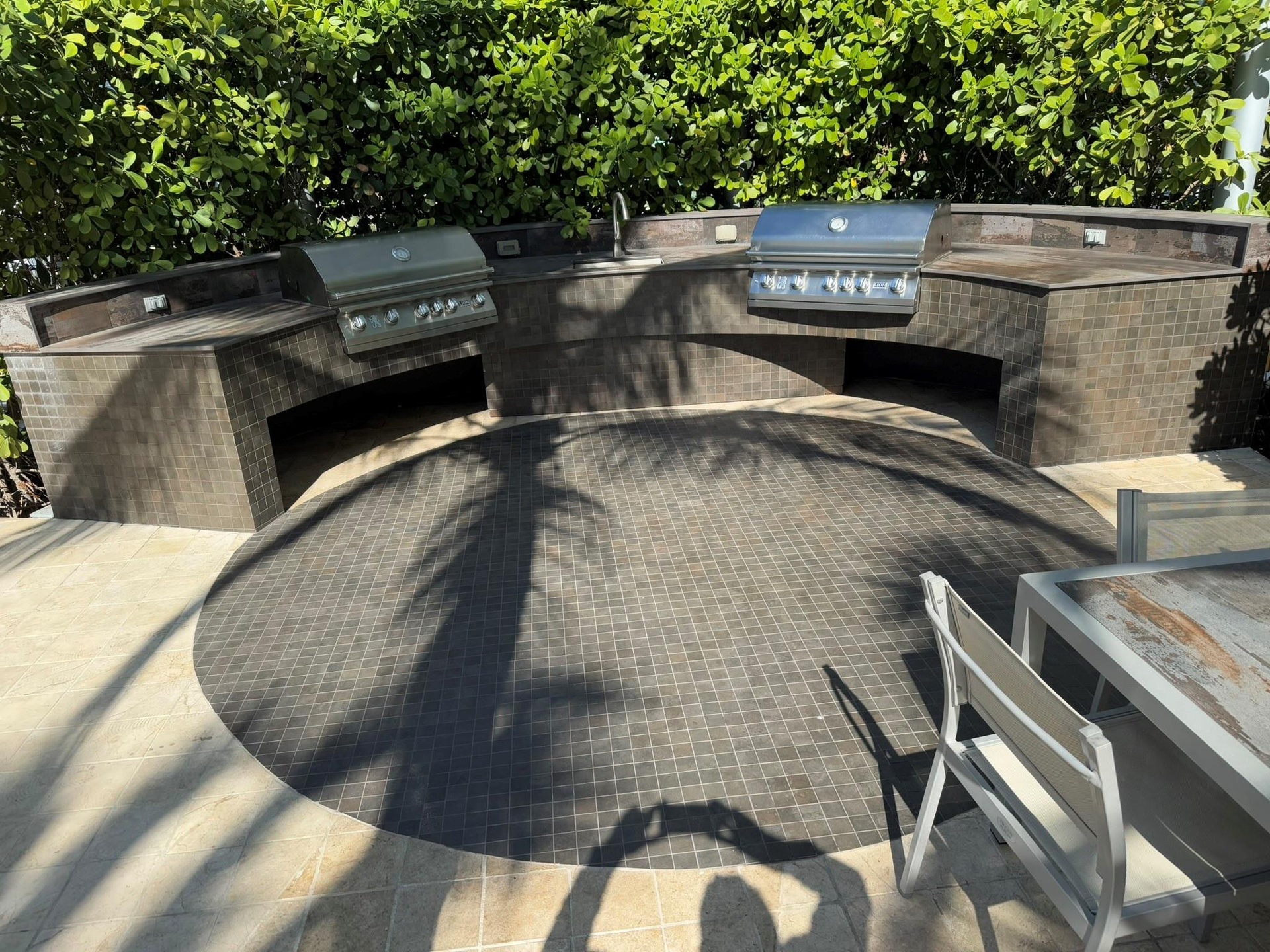 Outdoor kitchen with two built-in stainless steel grills, a sink, and integrated countertop lighting